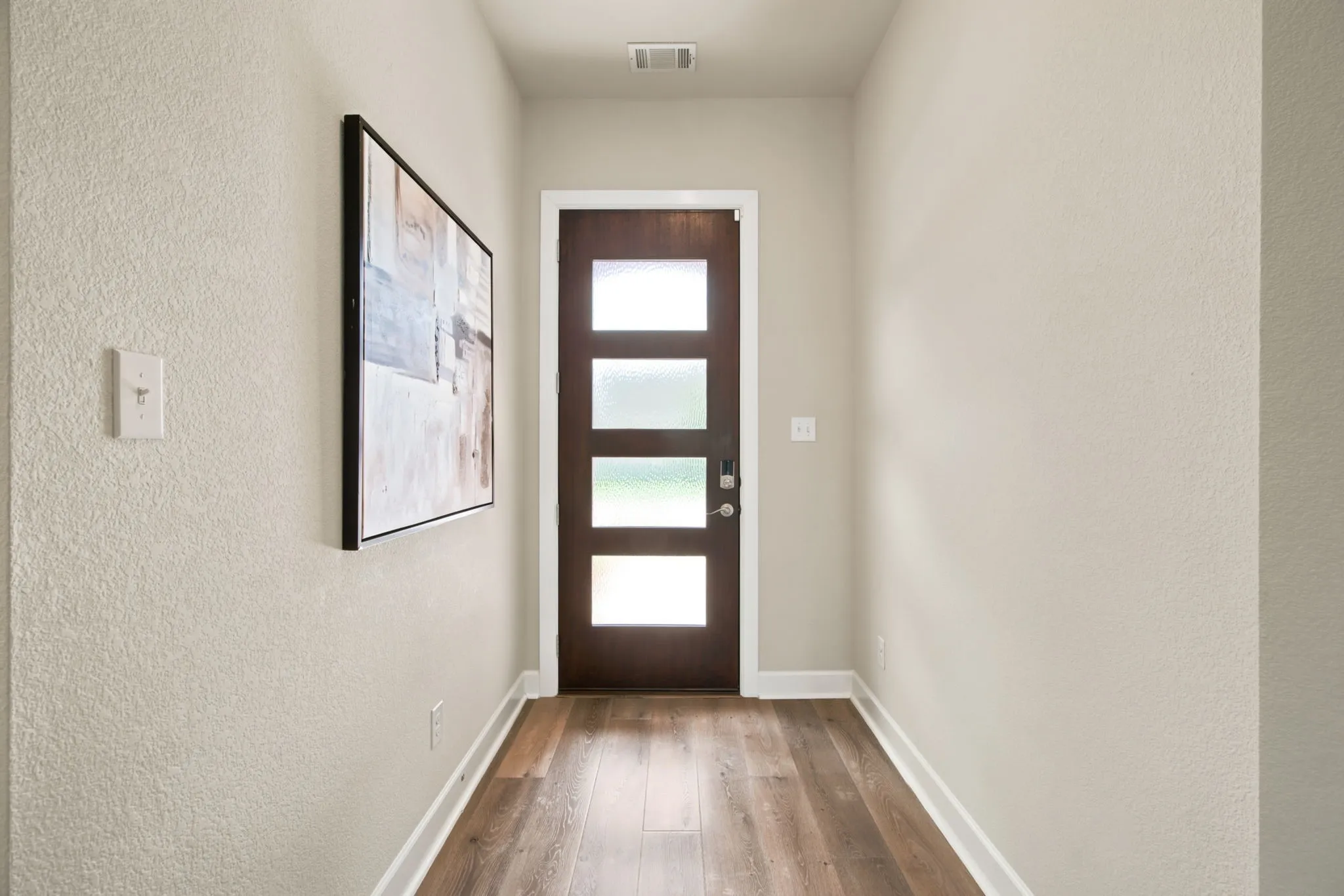 Entryway featuring a dark wood-finish door with four frosted glass panels, wood-finish flooring, and white baseboards