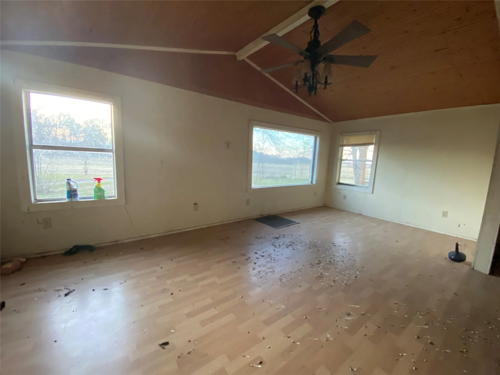 Spare room featuring vaulted ceiling with beams, light hardwood / wood-style flooring, ceiling fan, and a healthy amount of sunlight