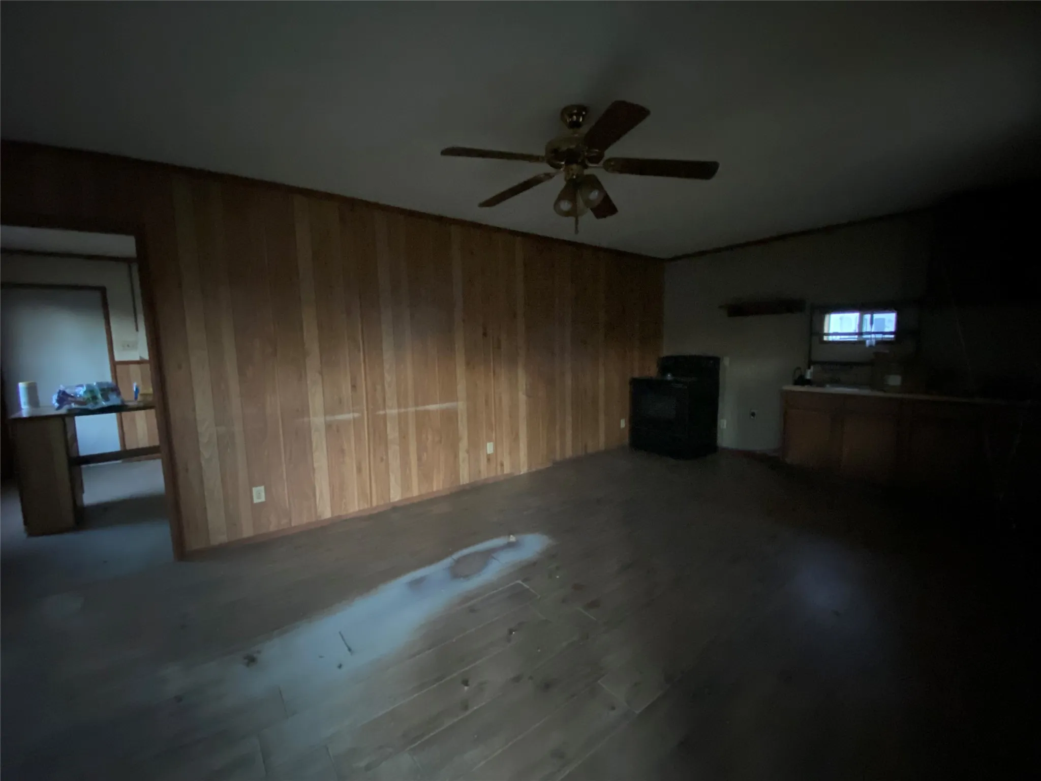 Unfurnished living room with ceiling fan, wood-type flooring, and wooden walls
