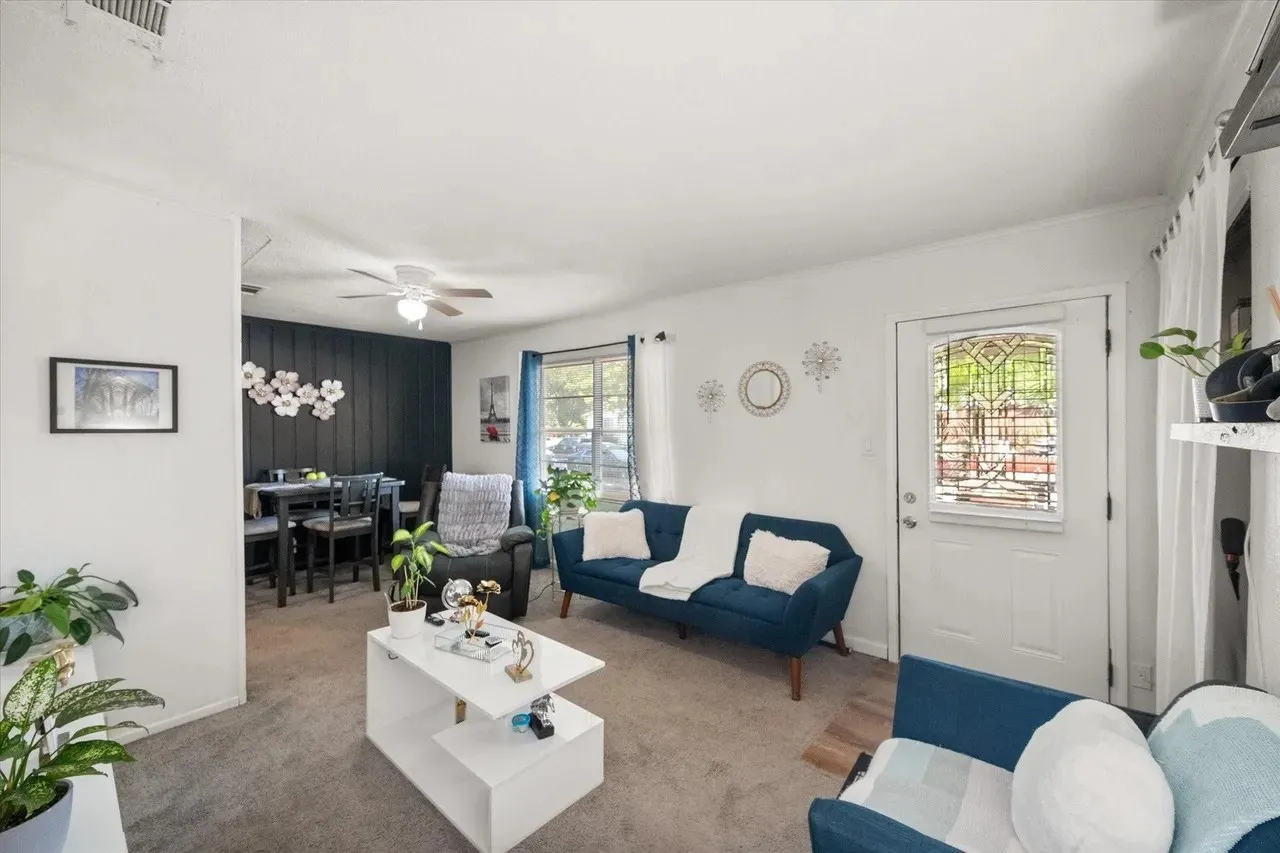 Spacious living area featuring carpet flooring, a ceiling fan, and a white entry door with a decorative glass insert