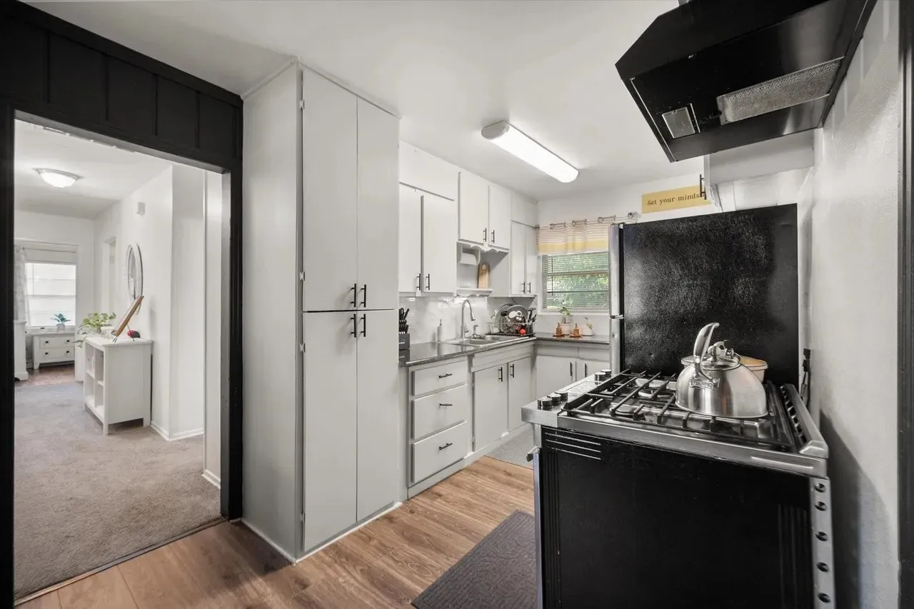 Kitchen featuring wood-finish flooring, light-toned cabinetry with dark hardware, dark countertops, and a gas range with an overhead vent