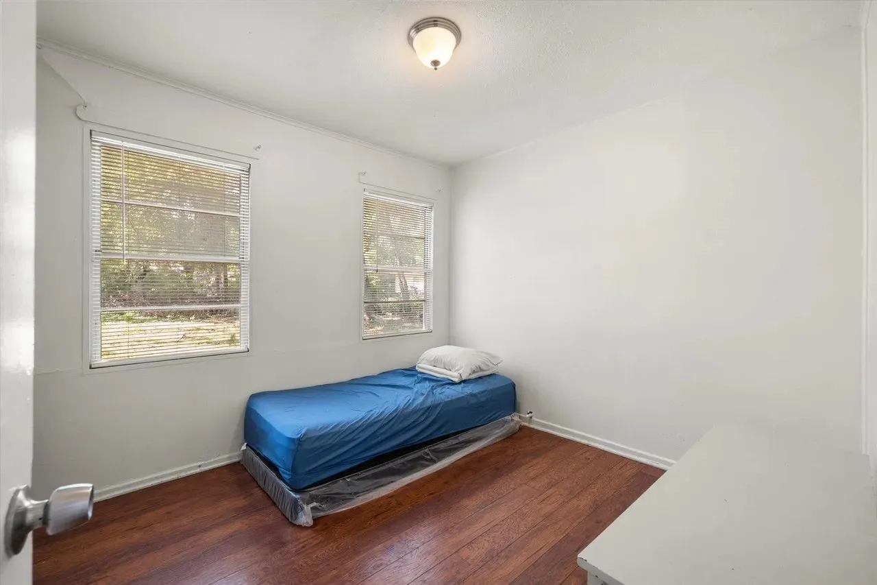 Room featuring wood-finish flooring, two windows with blinds, a white ceiling with a flush-mount light fixture, and white painted walls