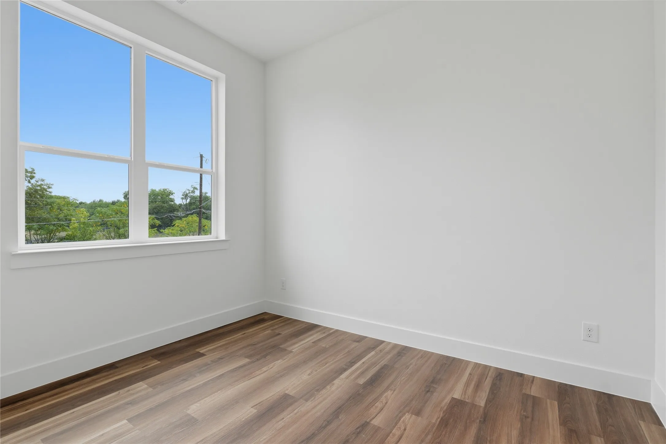 Spacious room featuring wood-finish flooring and a large window with white trim