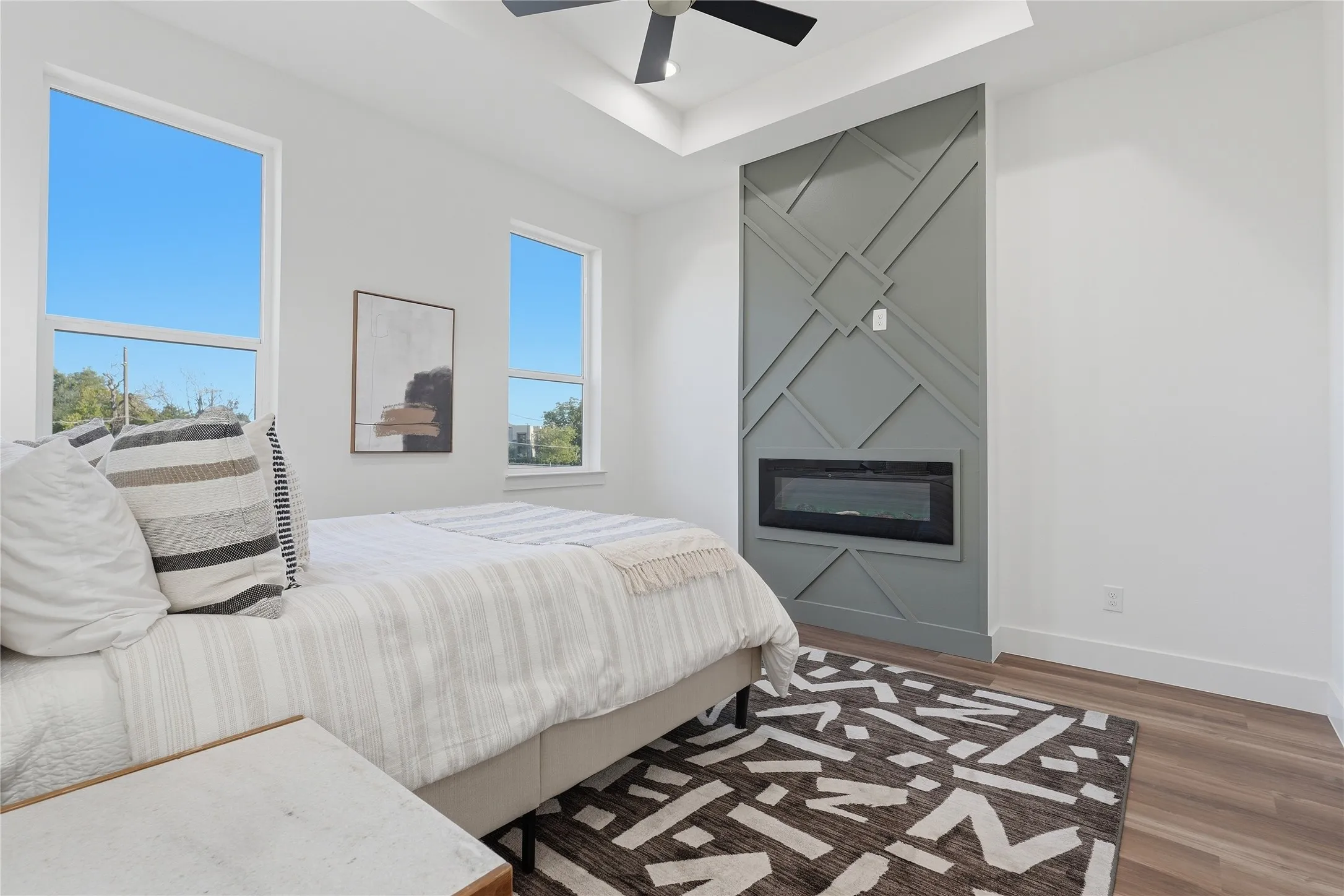 Recessed electric fireplace with a decorative accent wall, wood-finish flooring, and a ceiling fan
