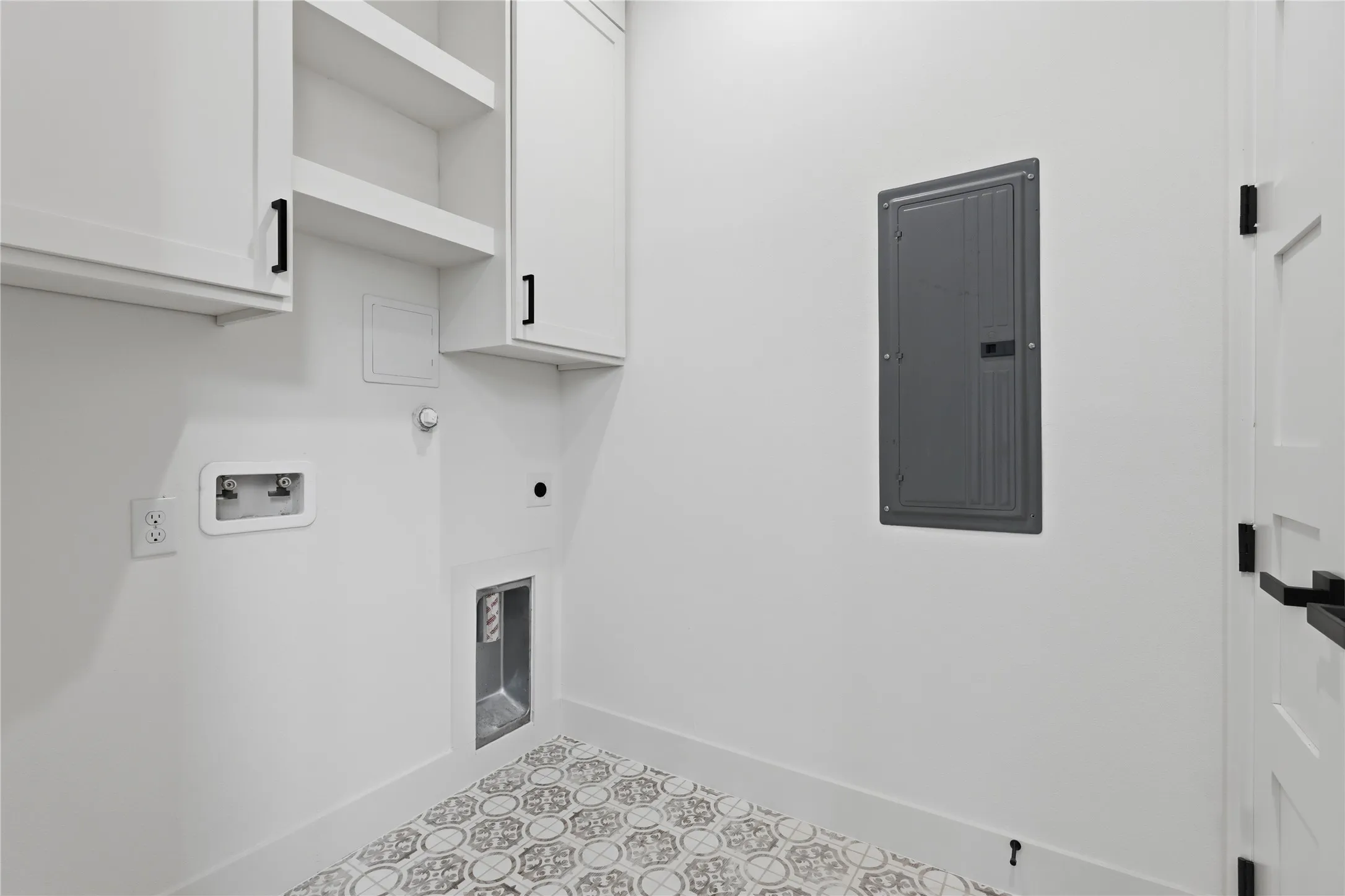 Utility space featuring patterned floor tiles, white cabinetry with matte black hardware, and an electrical panel