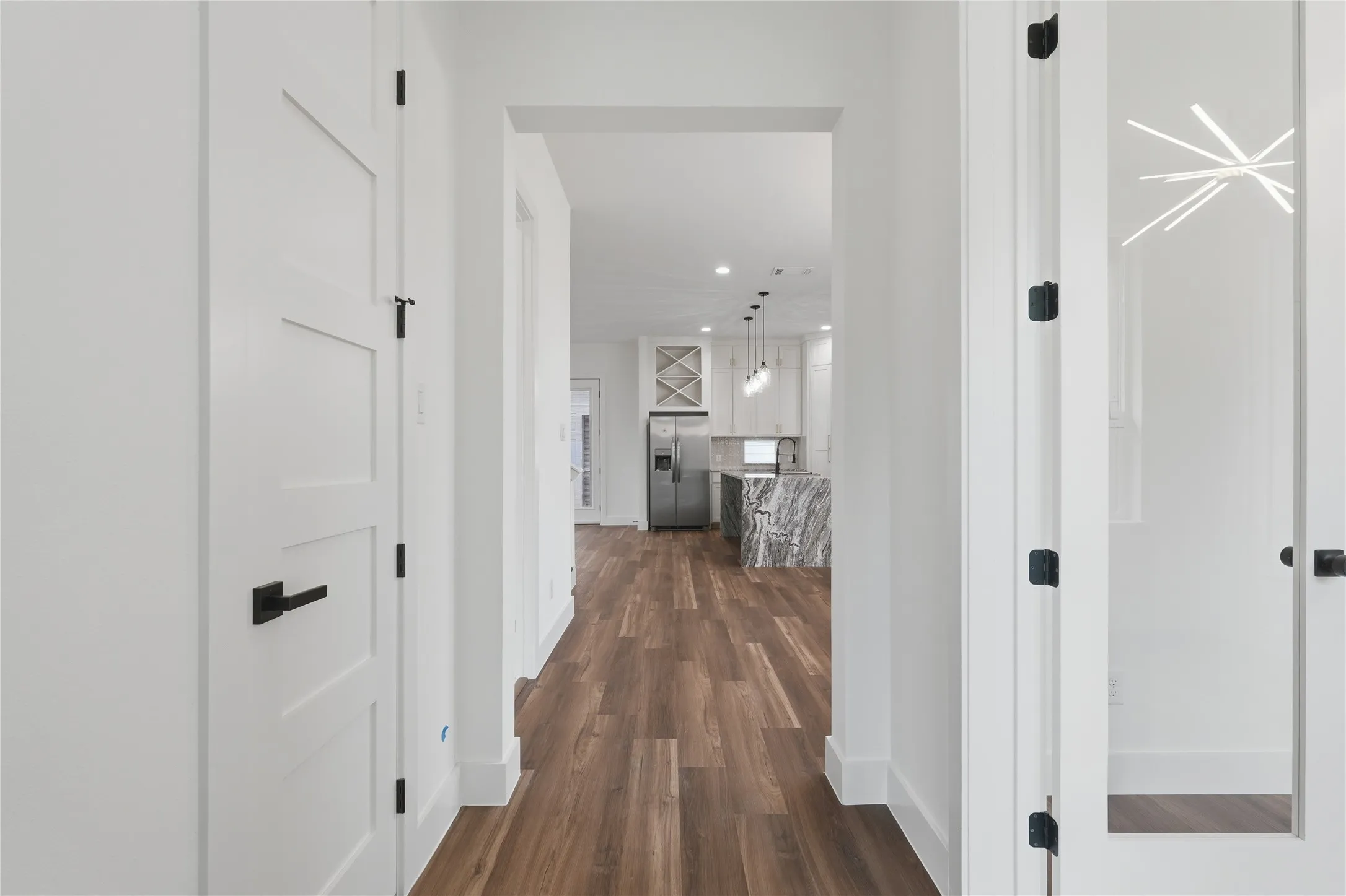 Hallway featuring wood-finish flooring, white walls, and contemporary black hardware on doors