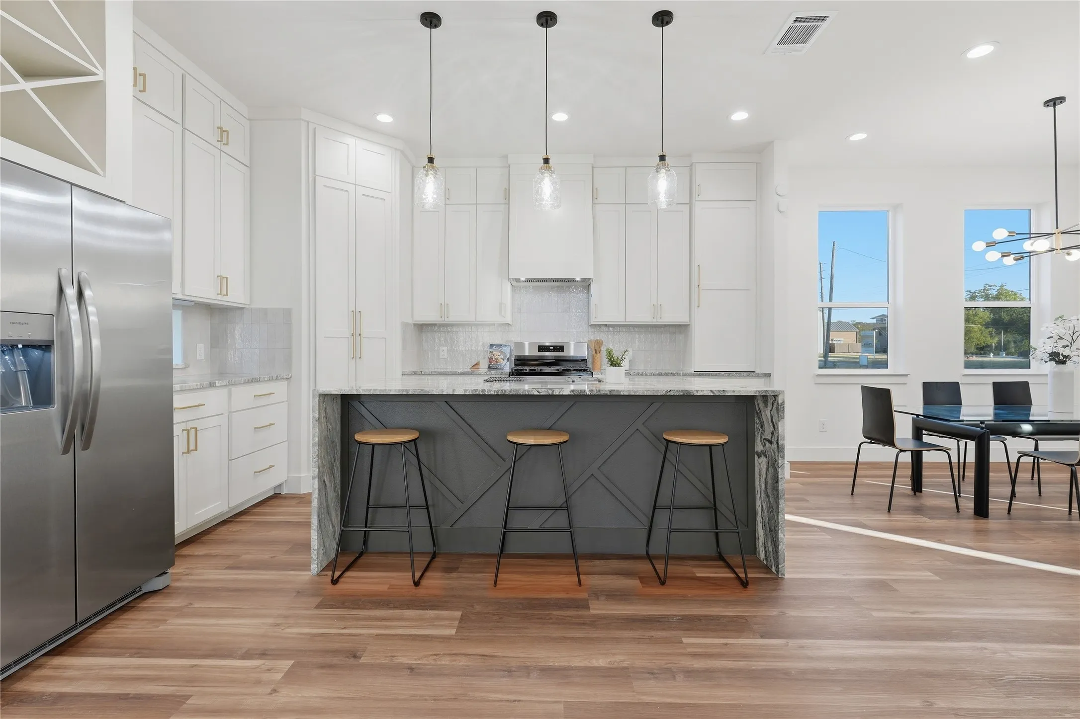 Gourmet kitchen featuring stainless steel appliances, a center island with bar seating, white shaker cabinetry, a stone slab backsplash, and wood-finish flooring