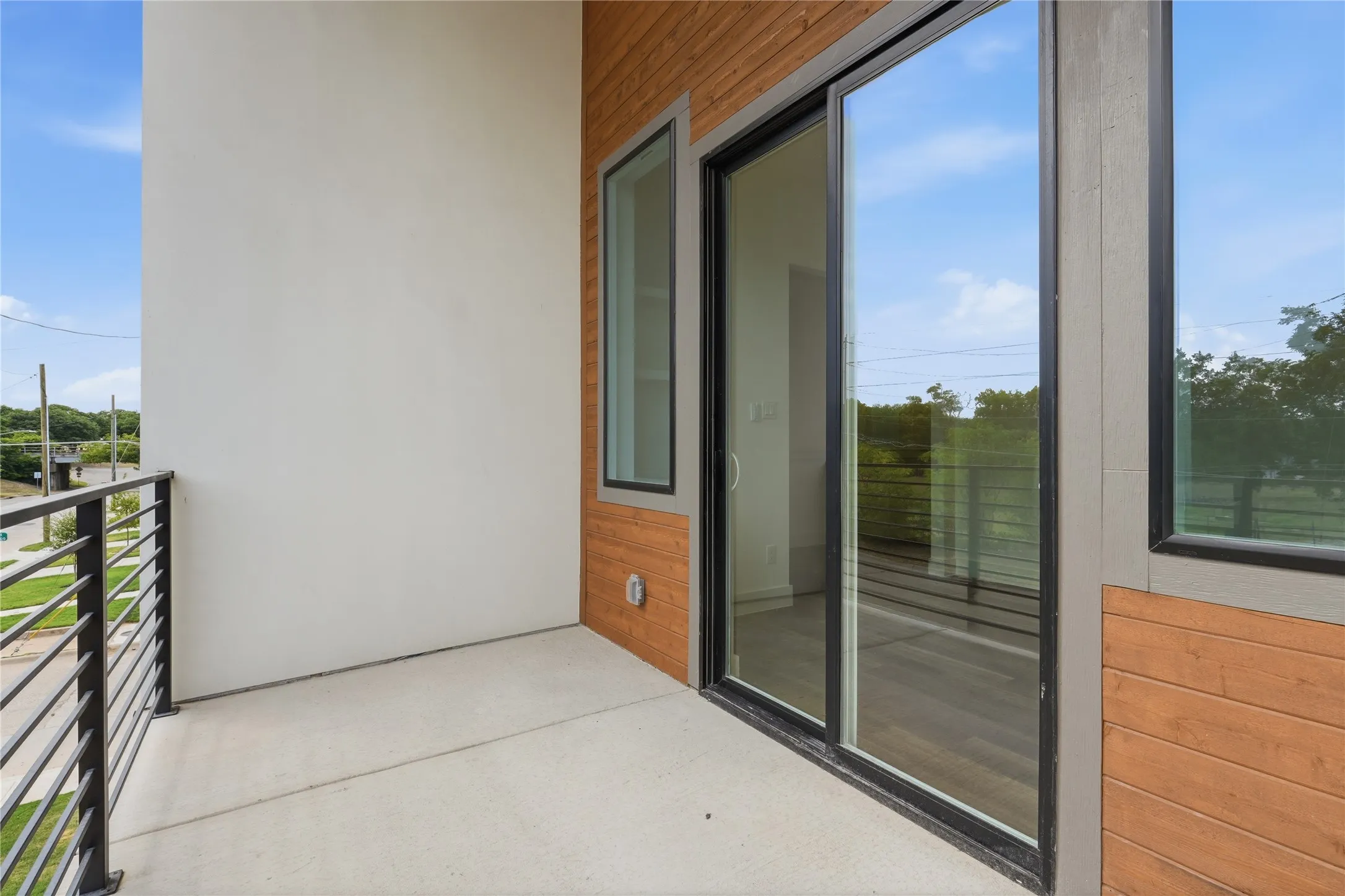 Concrete balcony featuring horizontal metal railings, wood-finish siding, and a large sliding glass door