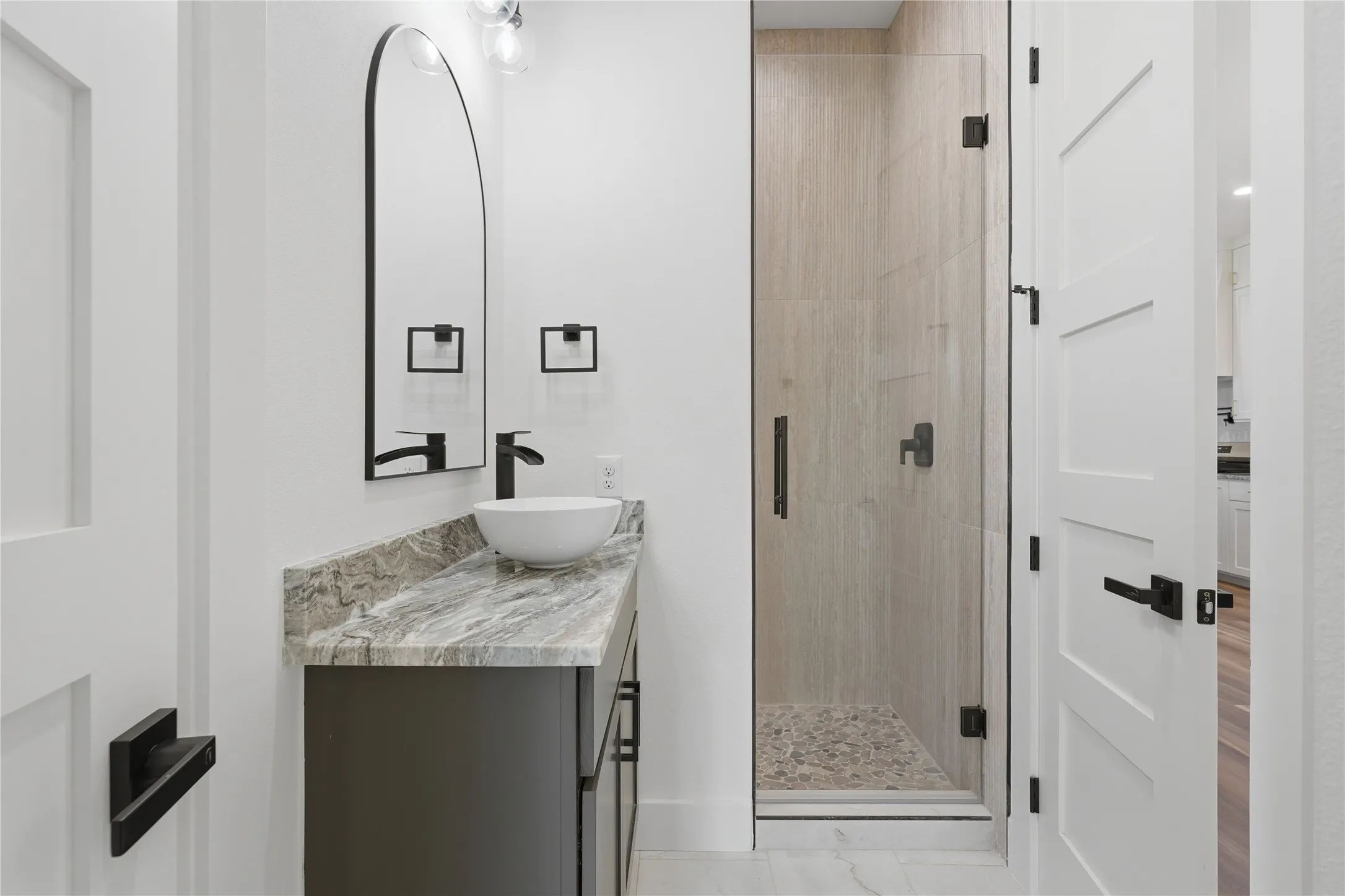 Bathroom featuring a contemporary floating vanity with a vessel sink, a stone countertop, a walk-in shower with a glass enclosure, and modern matte black fixtures