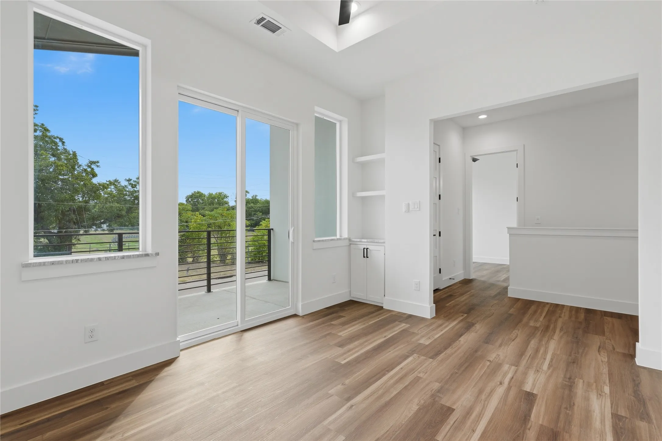 Wood-finish flooring, built-in shelving, sliding glass door, balcony, and large windows