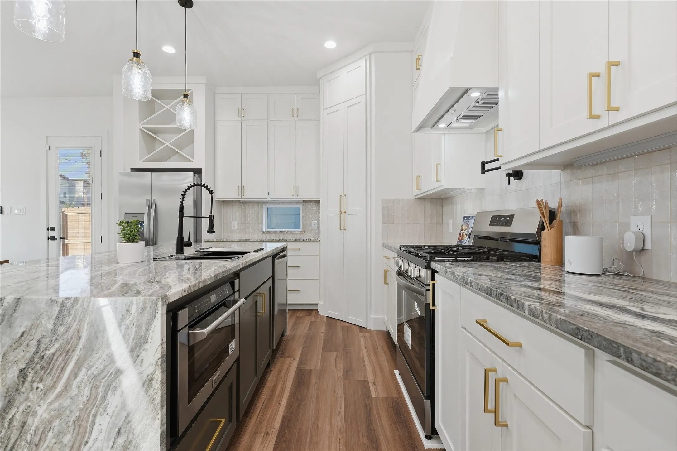 Kitchen featuring a central island with stone countertop, stainless steel appliances, wood-finish flooring, white cabinetry, and a tile backsplash