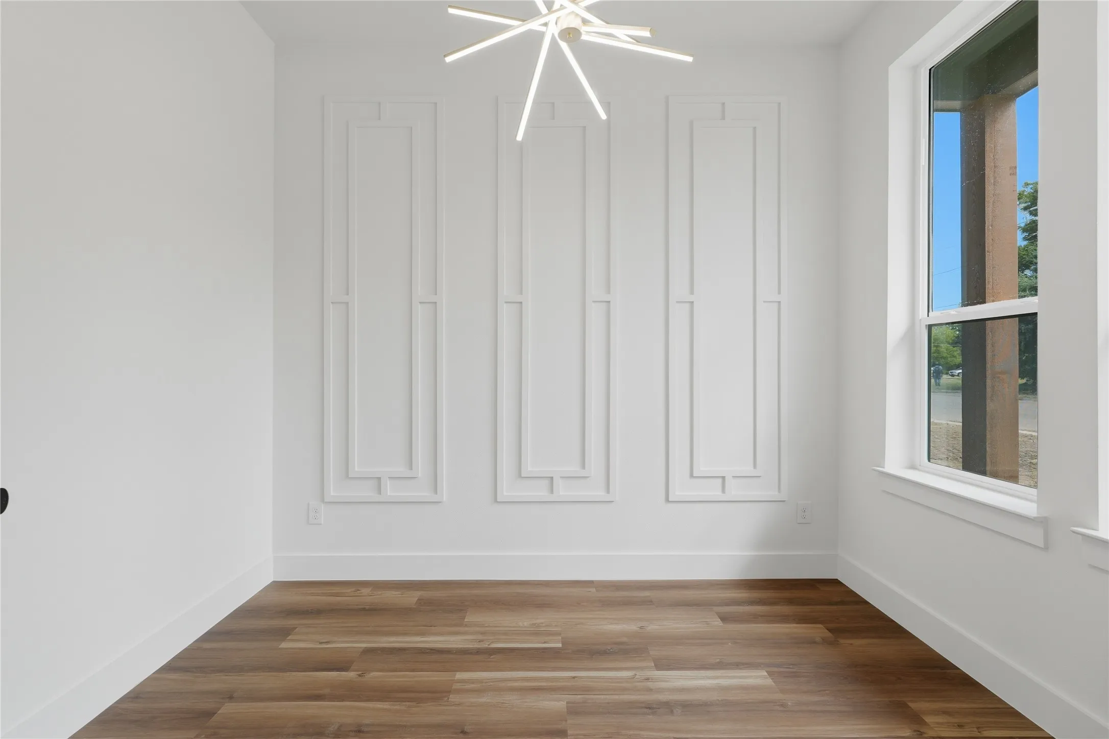Wood-finish flooring, white walls with decorative wall molding, and a modern linear chandelier