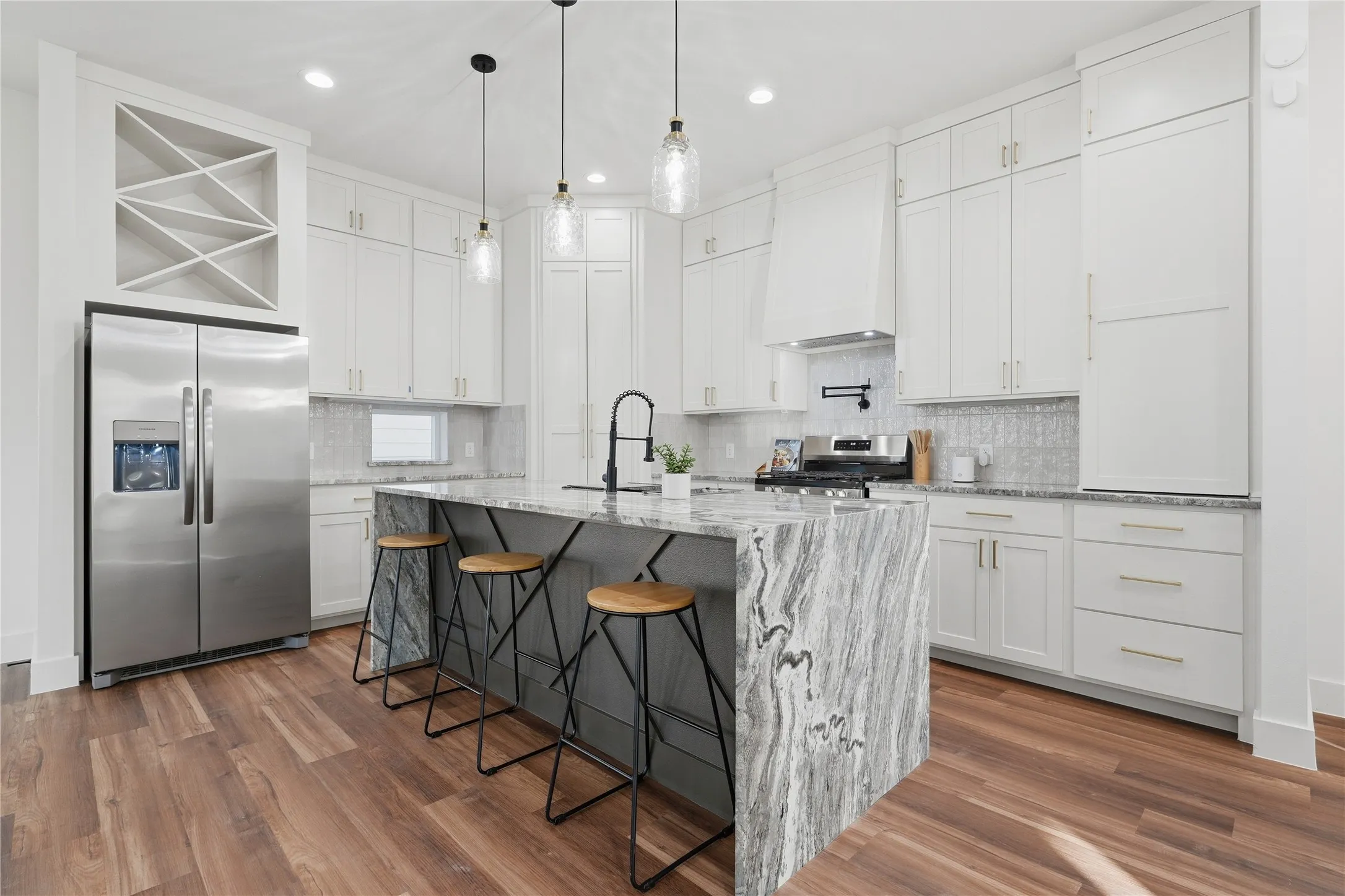 Kitchen featuring wood-finish flooring, white cabinetry, a large central island with a stone countertop, stainless steel appliances, and pendant lighting