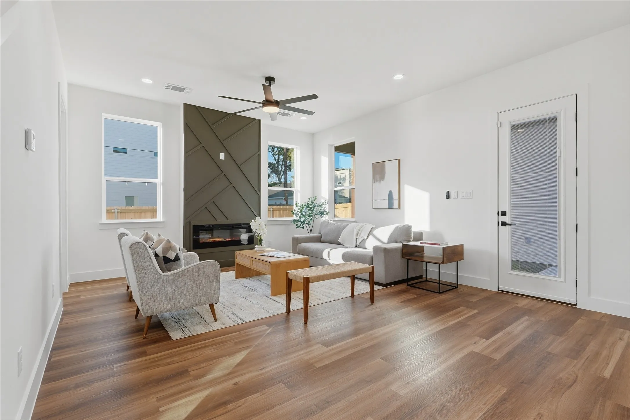 Wood-finish flooring, recessed lighting, and a linear electric fireplace with a geometric paneled accent wall