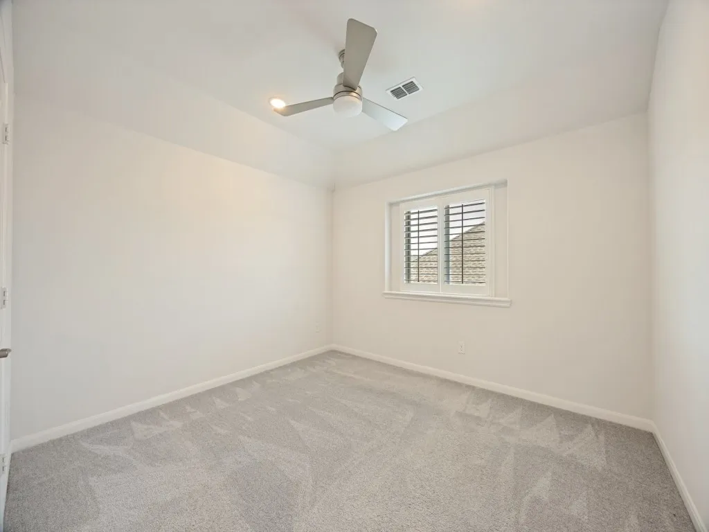 White-painted room featuring light gray carpet, a single window with white plantation shutters, and a ceiling fan with integrated lighting
