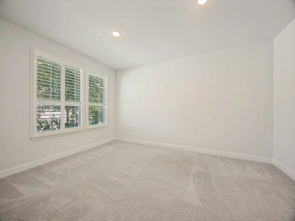 Bright and airy bedroom featuring expansive triple-pane windows with plantation shutters, recessed ceiling lighting, and neutral carpet flooring