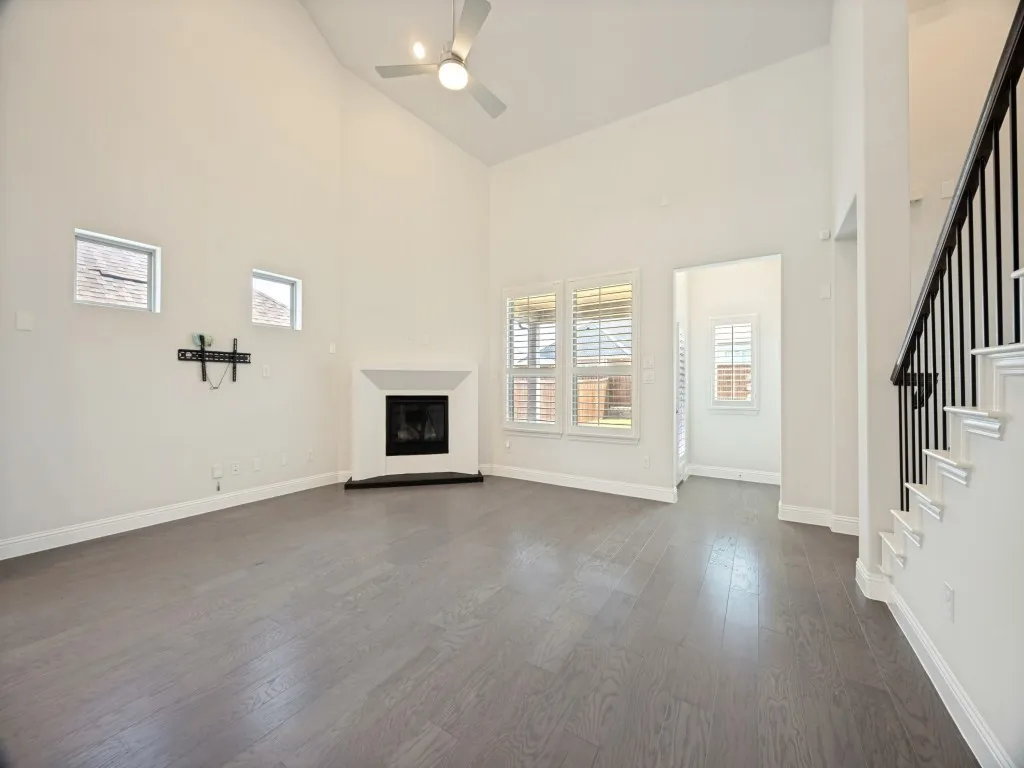 Spacious open-concept living area featuring soaring ceilings with ceiling fan, wood-finish flooring, and a corner fireplace with black surround