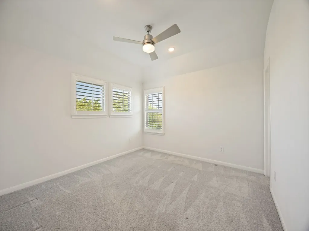 Carpeted interior space featuring multiple windows with plantation shutters, a ceiling fan with integrated lighting, and recessed ceiling lighting