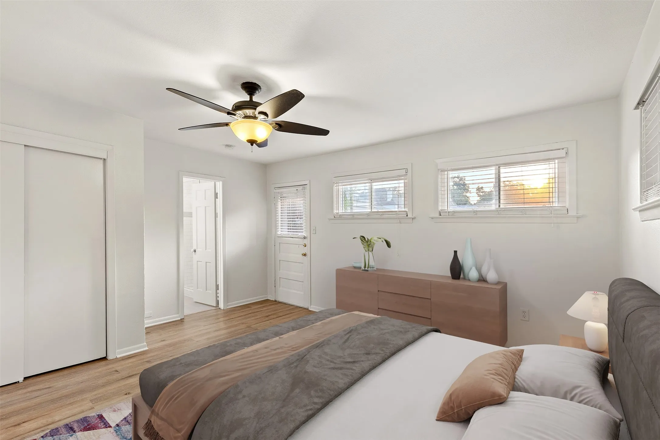 Wood-finish flooring, white walls, ceiling fan with integrated lighting, multiple windows with blinds, and a sliding closet door