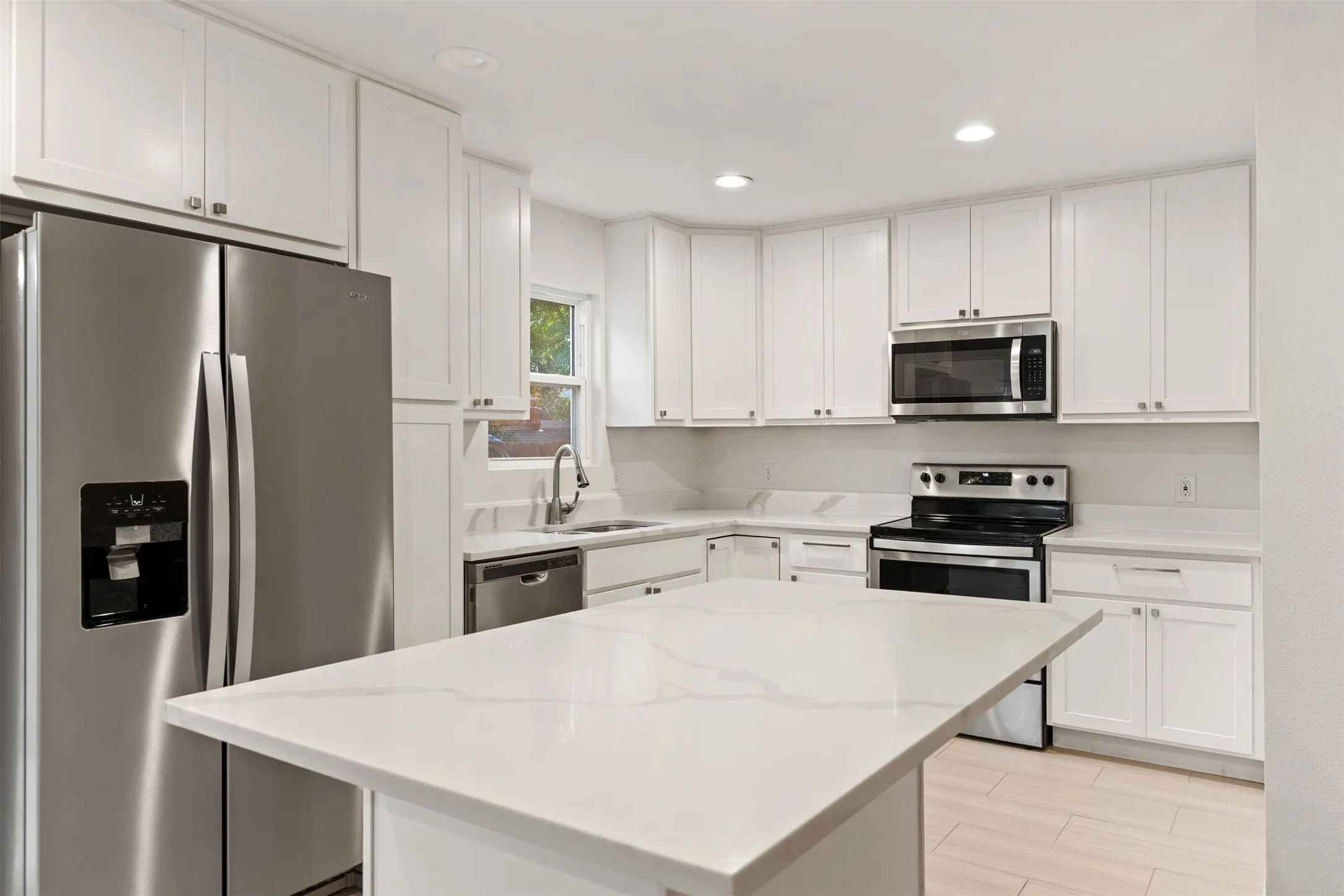 White shaker cabinetry, stainless steel appliances, quartz countertops, central island, and wood-finish flooring
