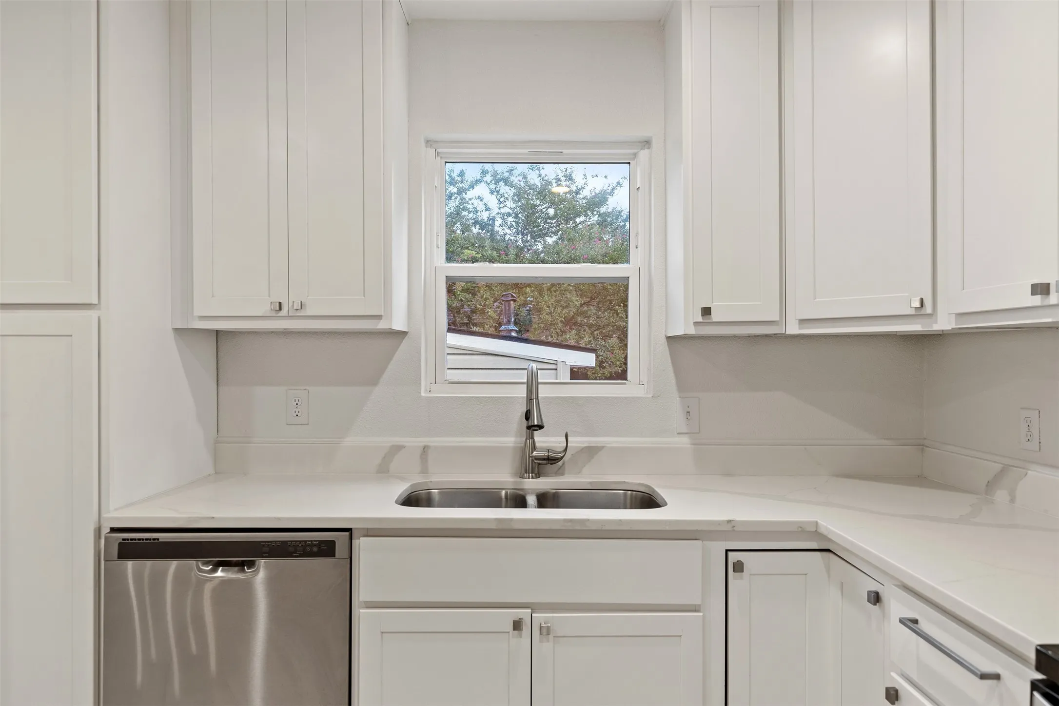 White shaker cabinetry with modern hardware, stainless steel sink, pull-down faucet, and white countertops