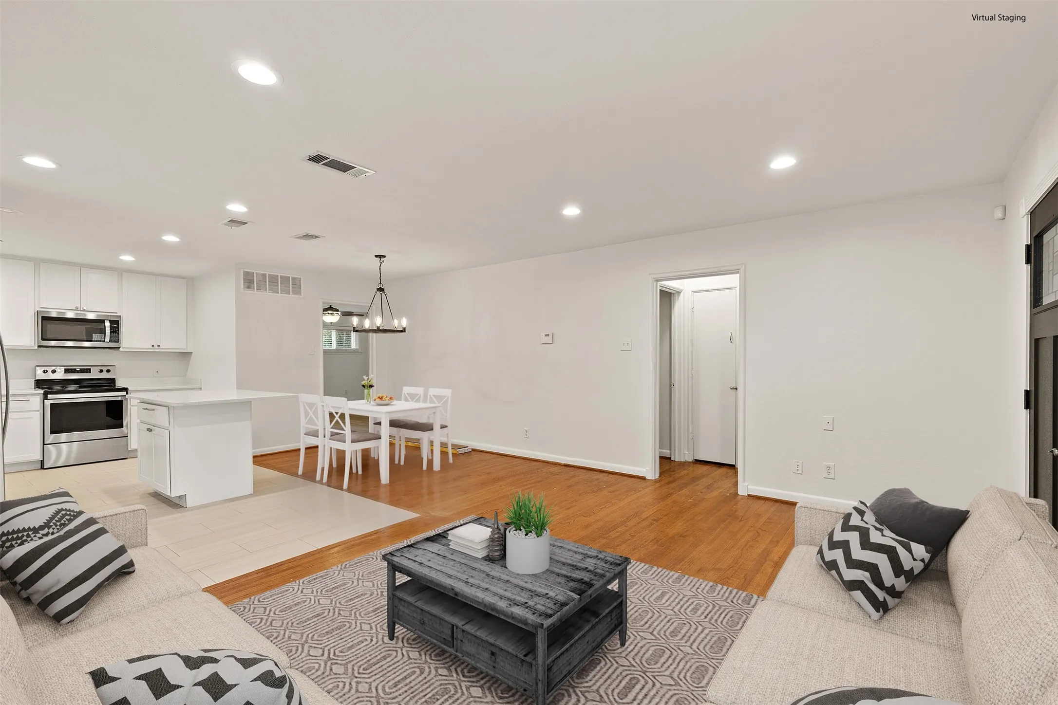 Open-concept living area featuring wood-finish flooring, white walls, recessed lighting, and a kitchen with stainless steel appliances and white cabinetry