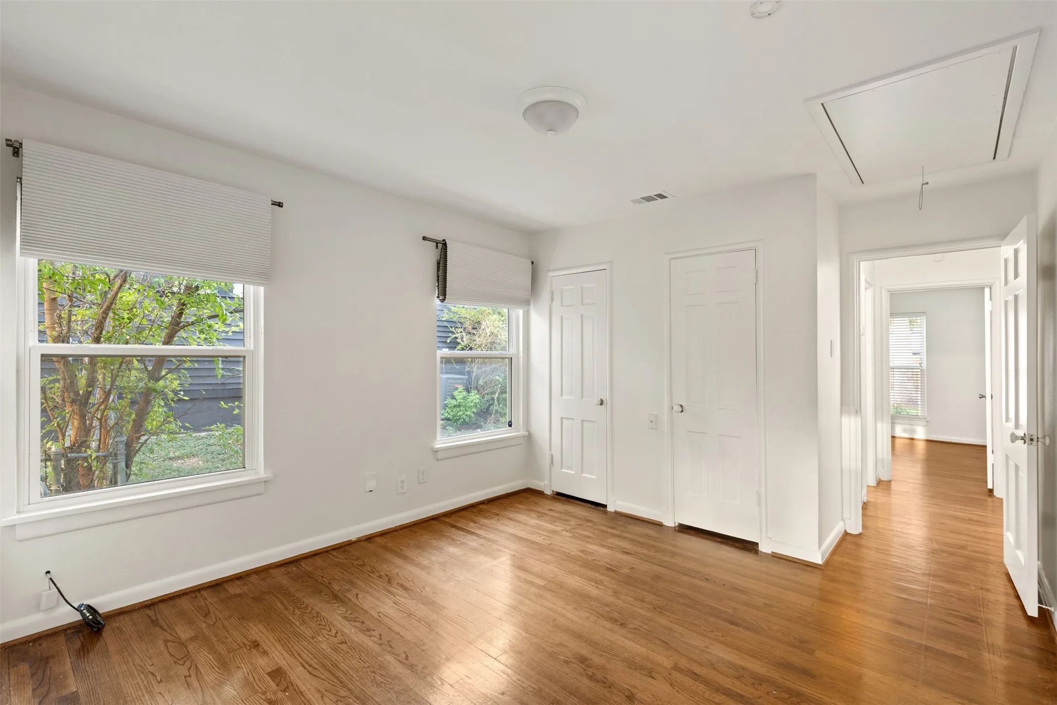 Hardwood flooring throughout, two windows with window treatments, two solid-panel interior doors, and overhead lighting