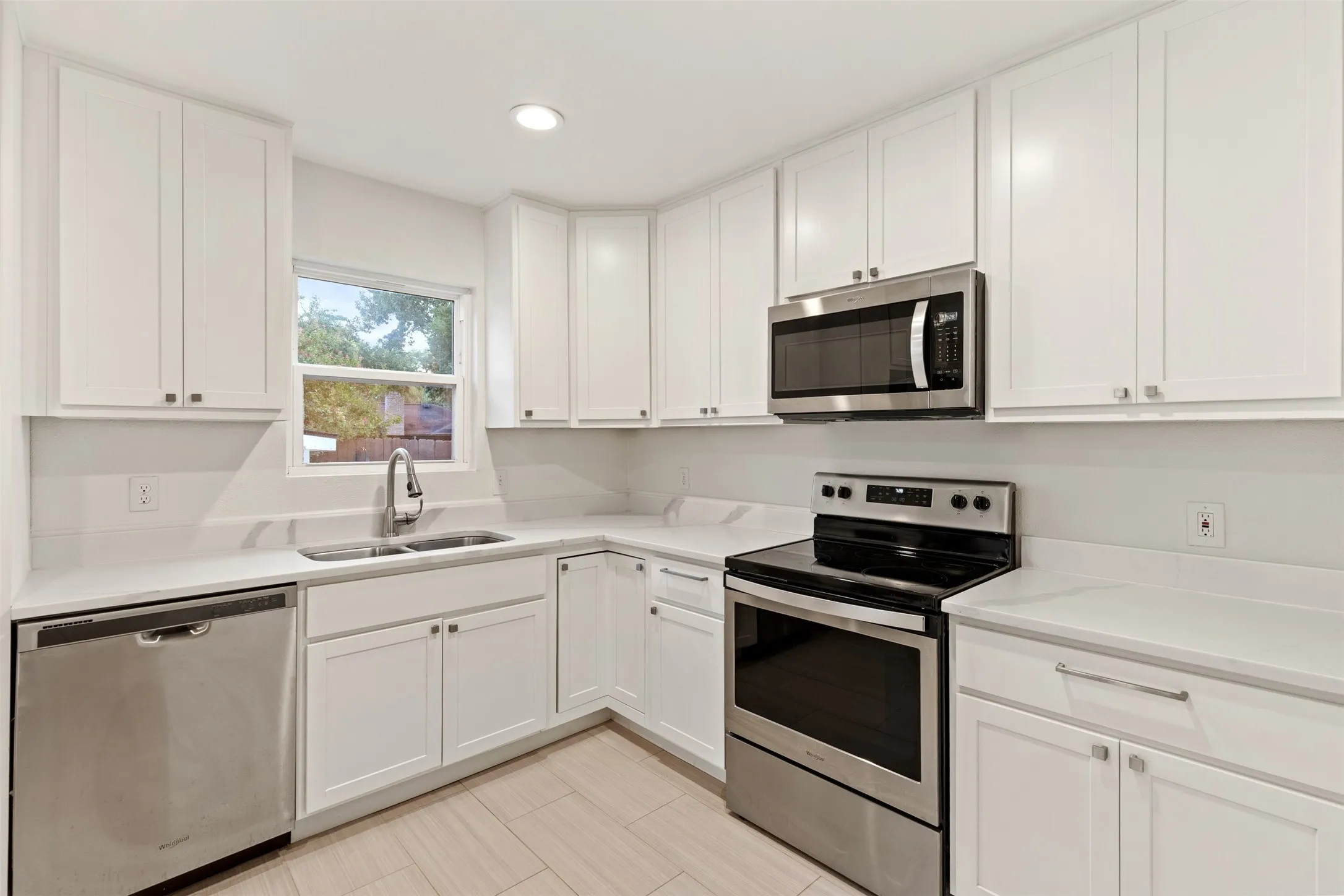 Crisp white cabinetry, stainless steel appliances, a corner window, light countertops, and wood-finish flooring