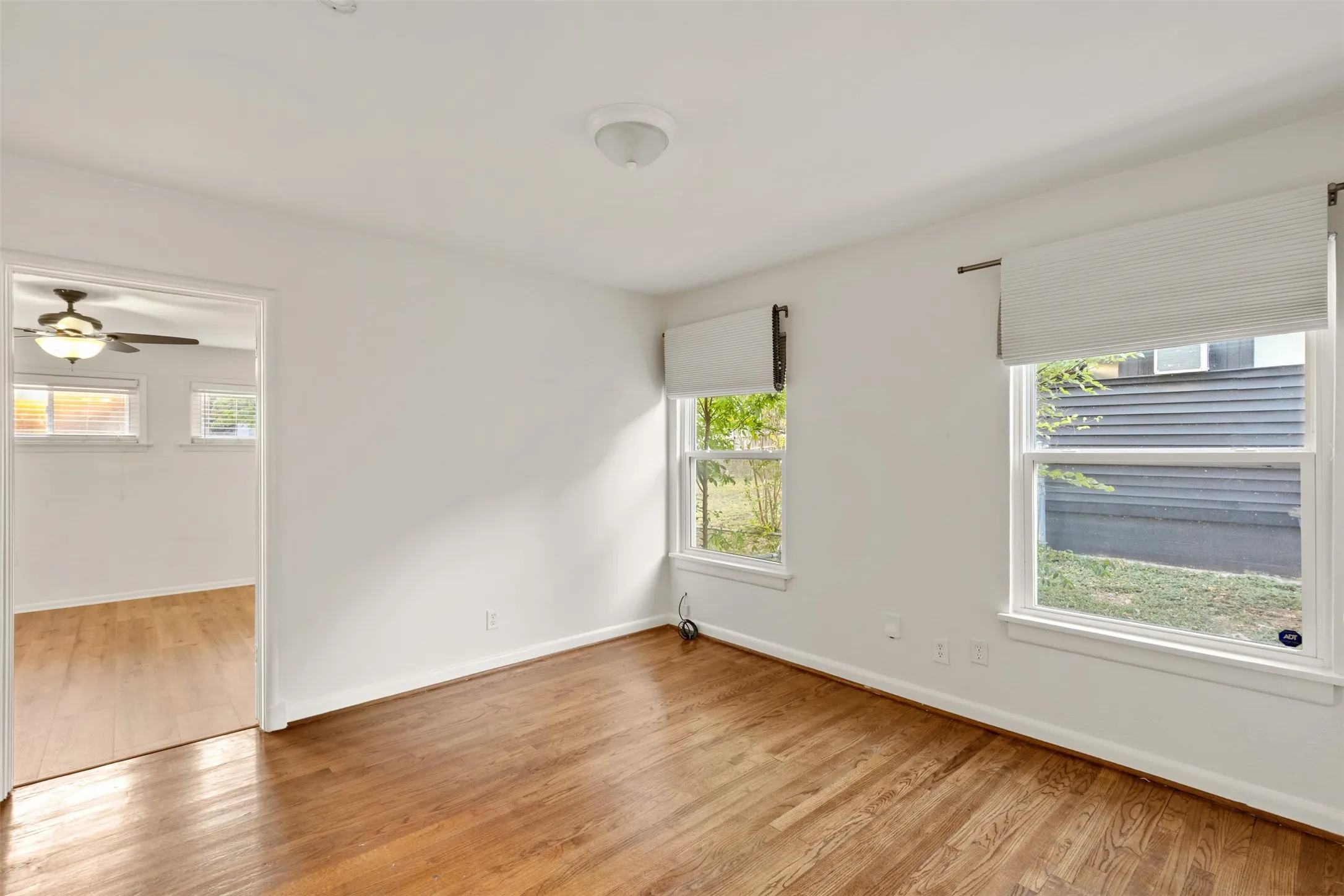 Hardwood flooring, white walls, multiple windows with blinds, ceiling-mounted light fixture