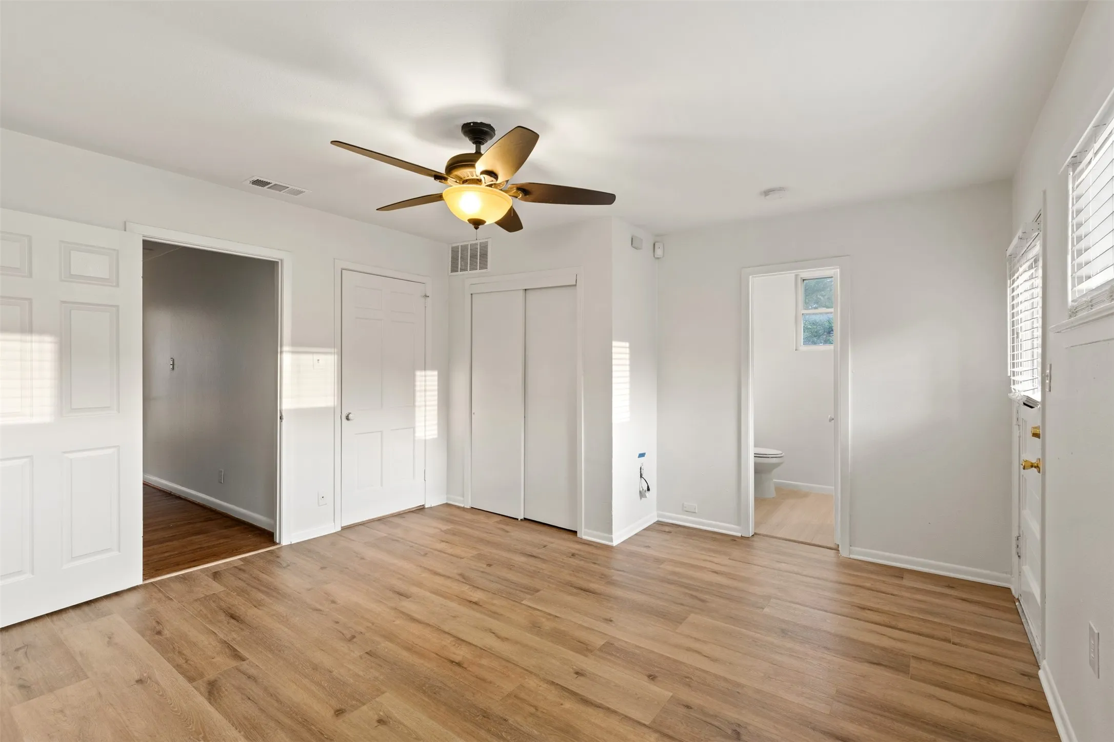 Wood-finish flooring, ceiling fan with integrated lighting, white paneled doors, and white walls