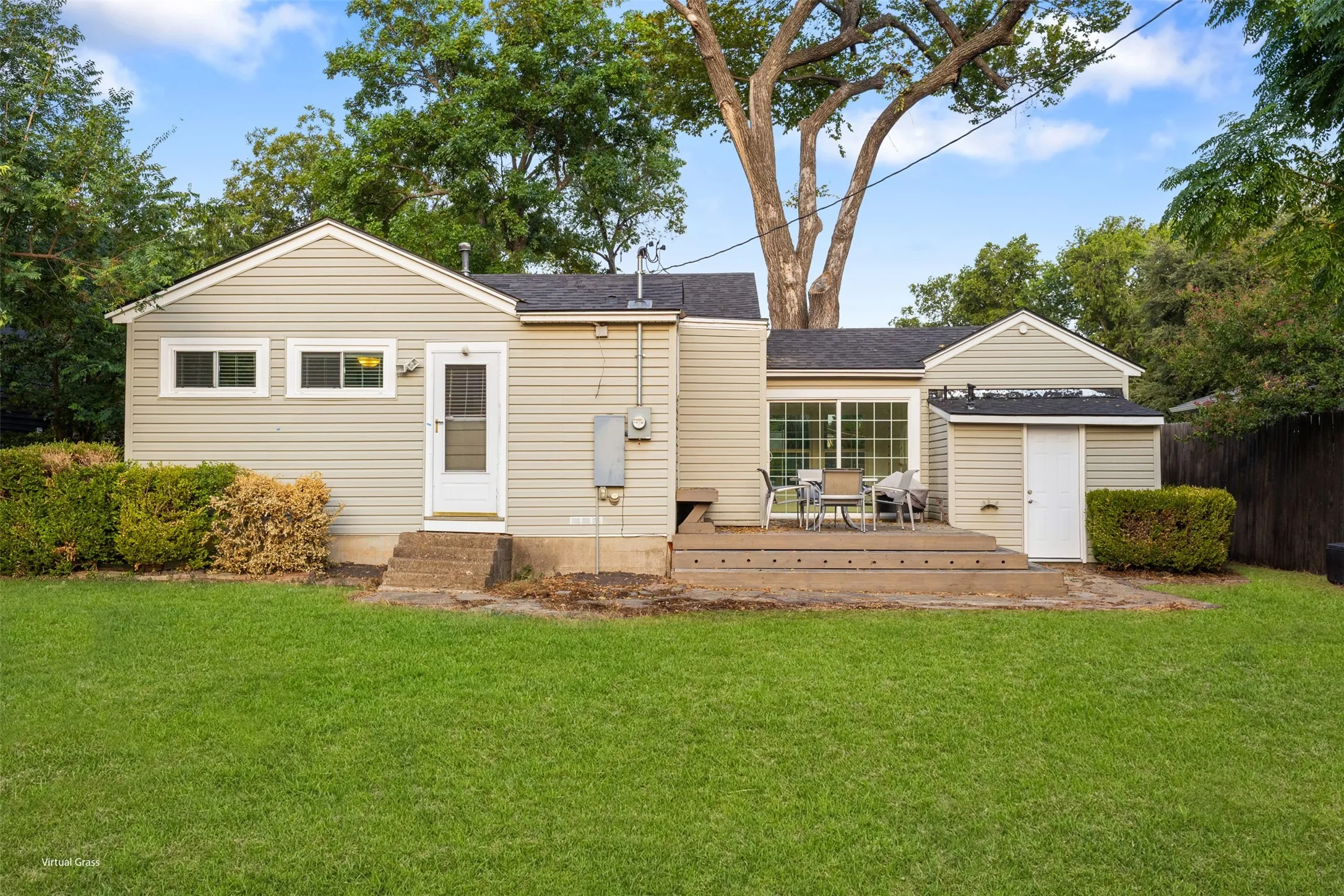 Expansive green lawn, light-colored siding, and a wooden deck with sliding glass doors