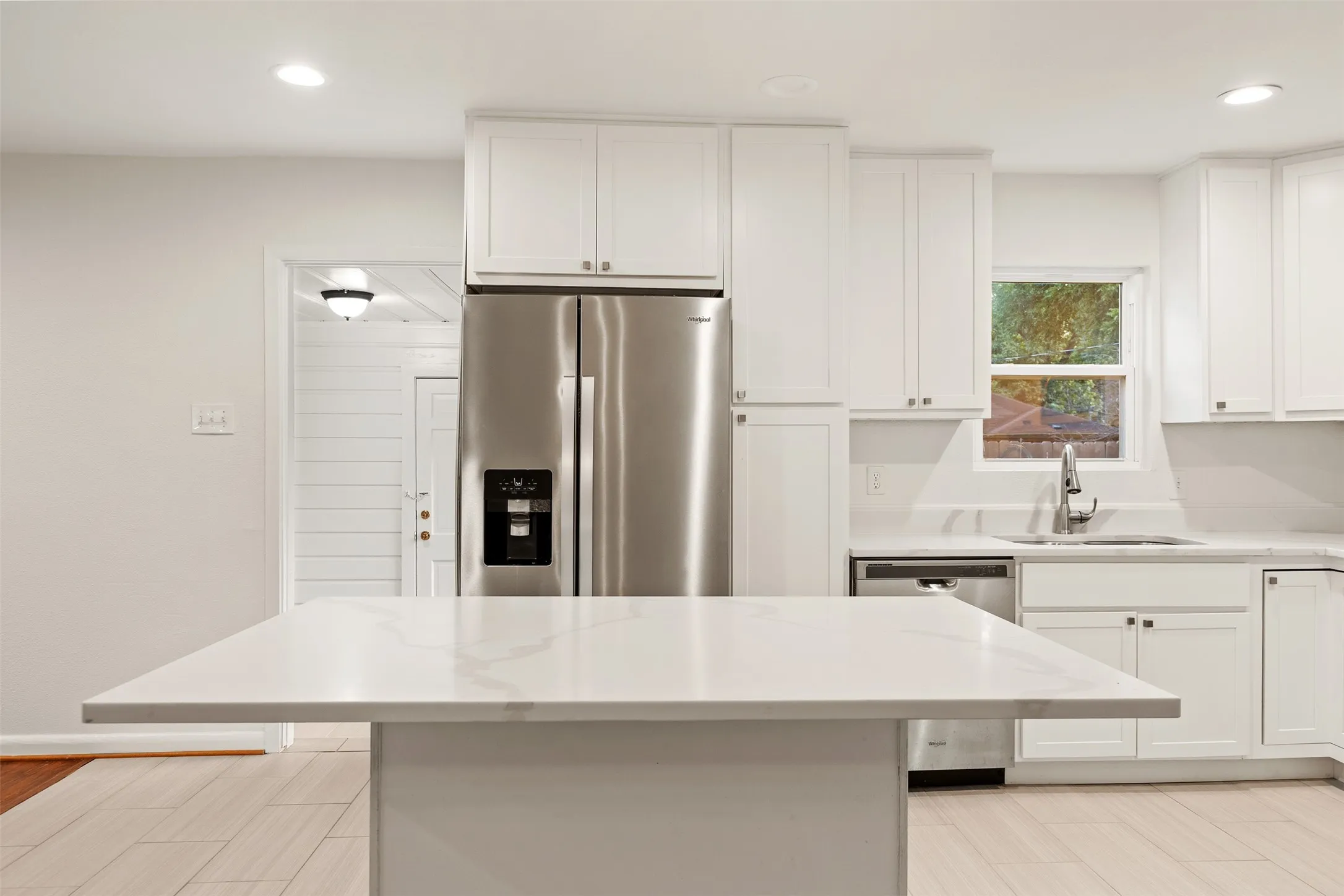 Kitchen featuring a central island with a light-toned countertop, stainless steel refrigerator, white cabinetry, undermount sink, and wood-finish flooring