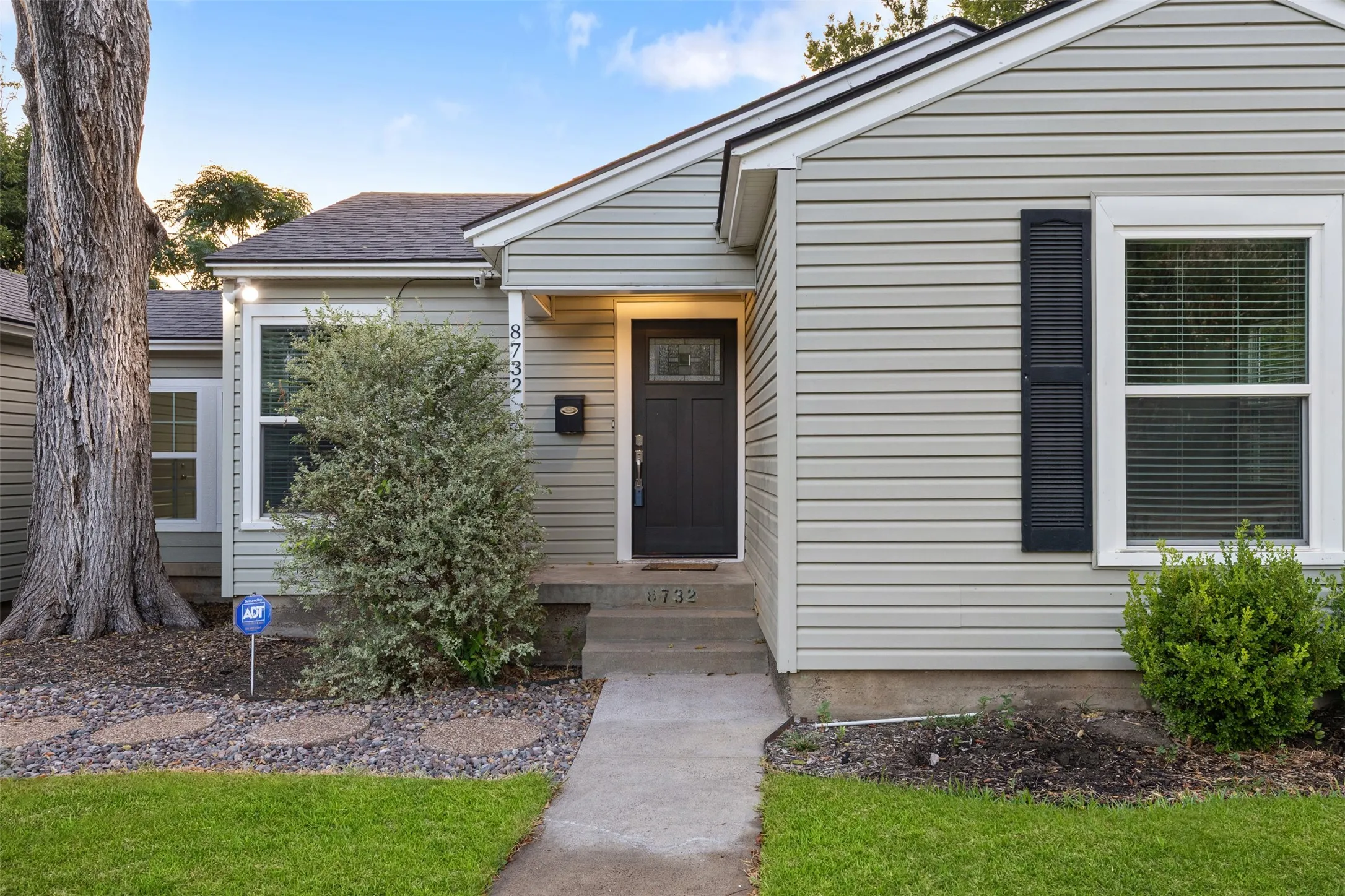 Light-colored siding exterior with a dark entry door, white trim windows, and dark shutters