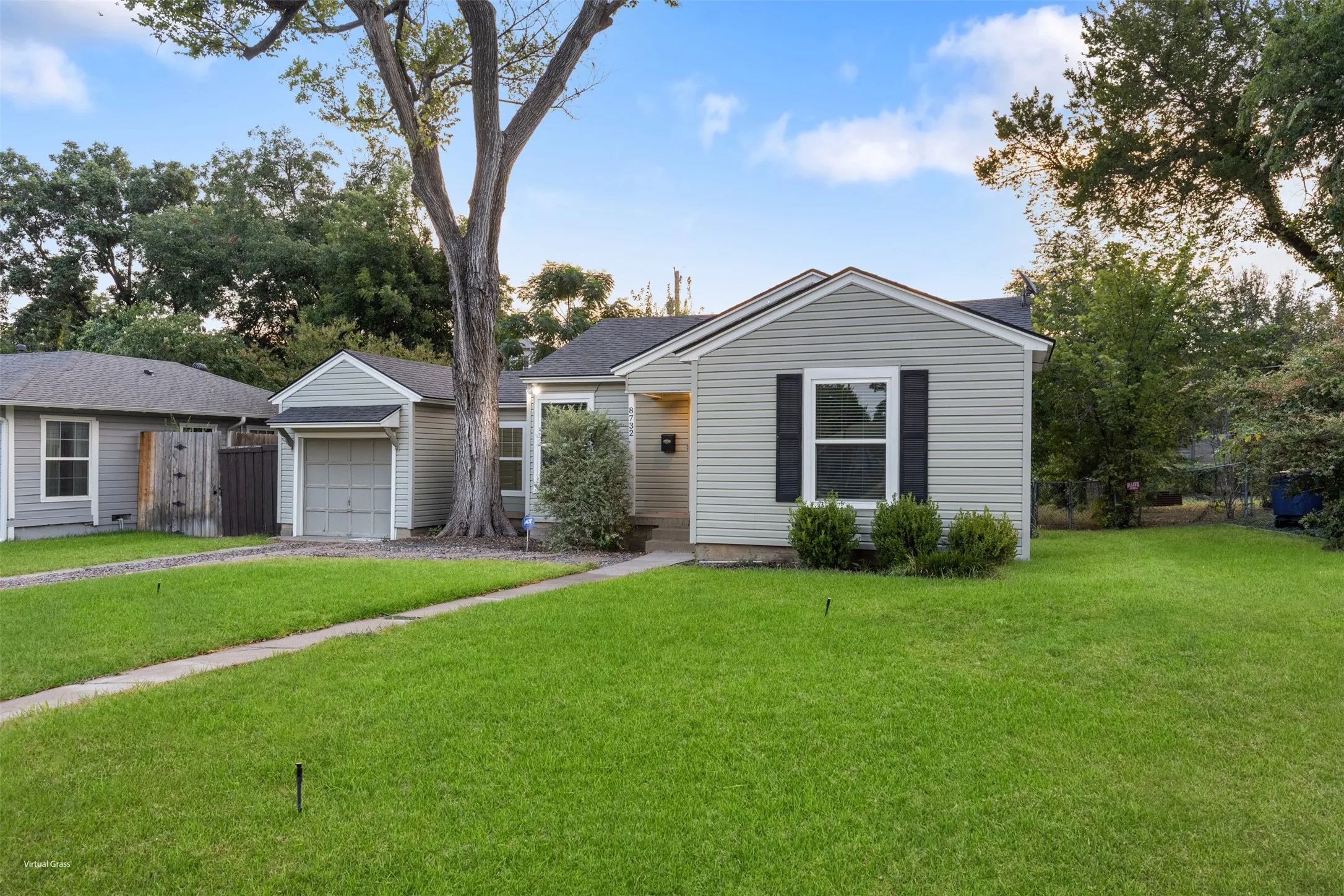 Exterior featuring gray siding, a single-car garage, black window shutters, a concrete driveway, and mature landscaping