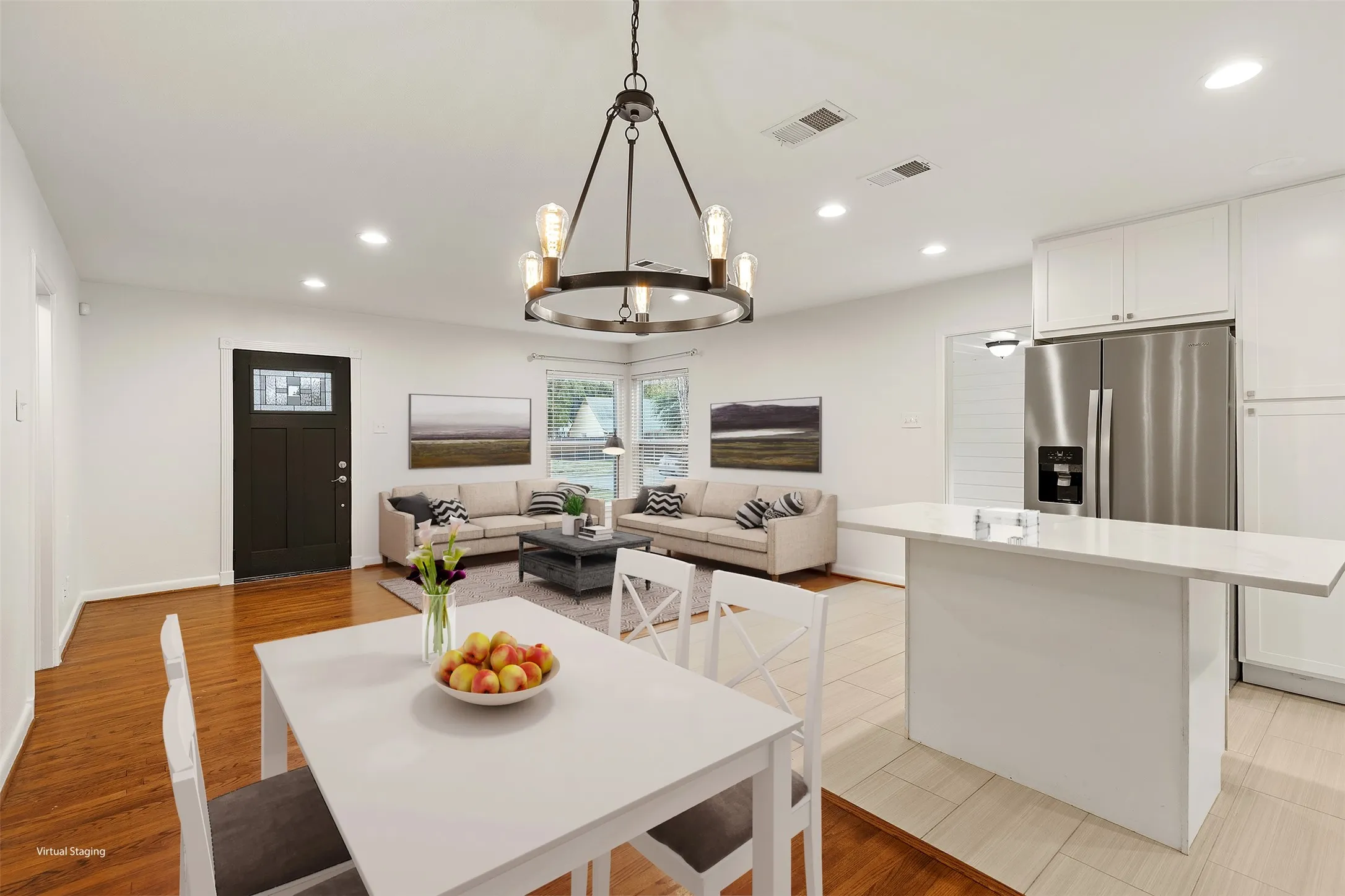 Open-concept living space featuring wood-finish flooring, recessed lighting, a kitchen island with seating, white cabinetry, and stainless steel appliances