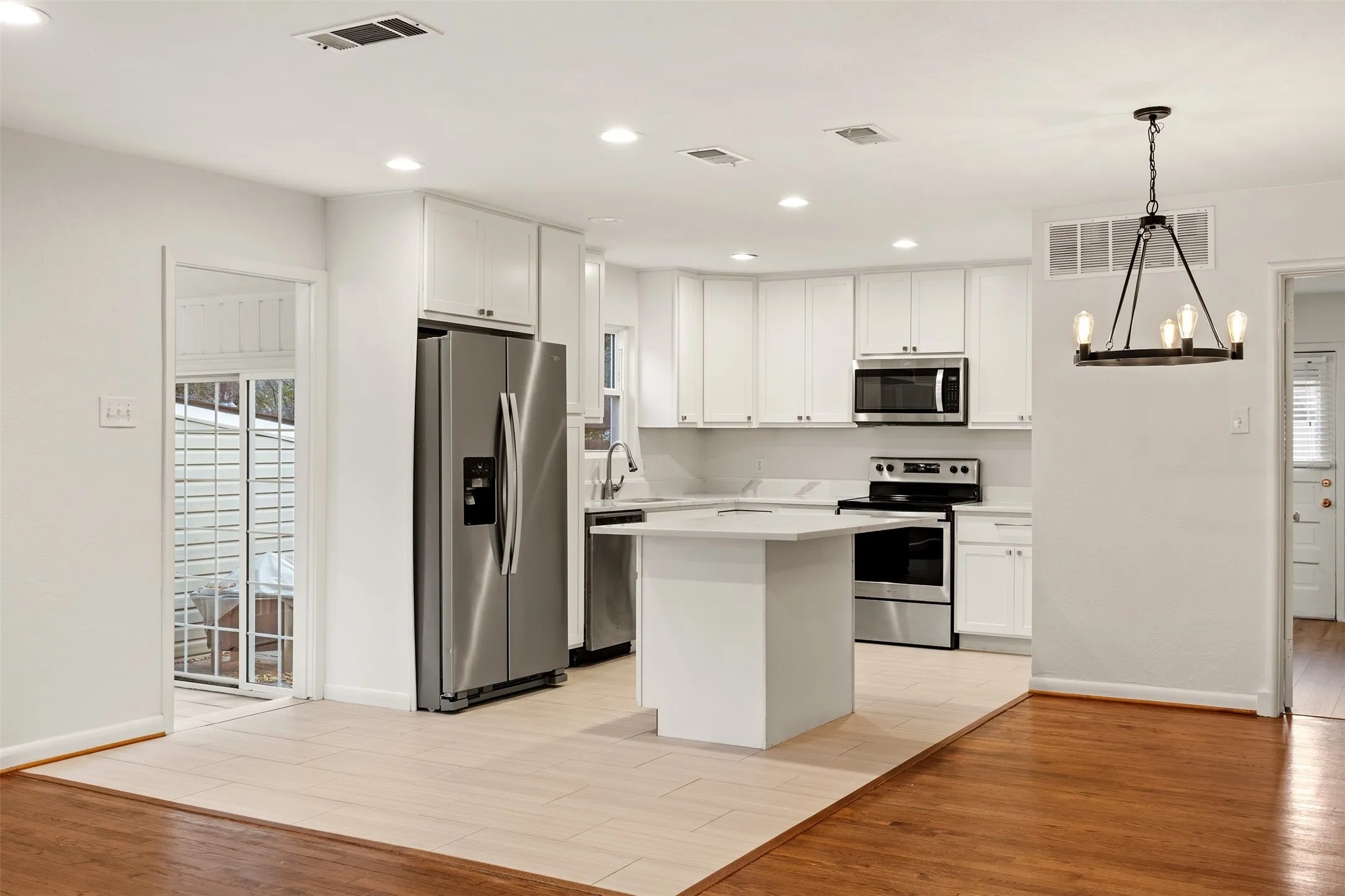Modern kitchen featuring stainless steel appliances, white cabinetry, a central island, recessed lighting, and a contemporary chandelier