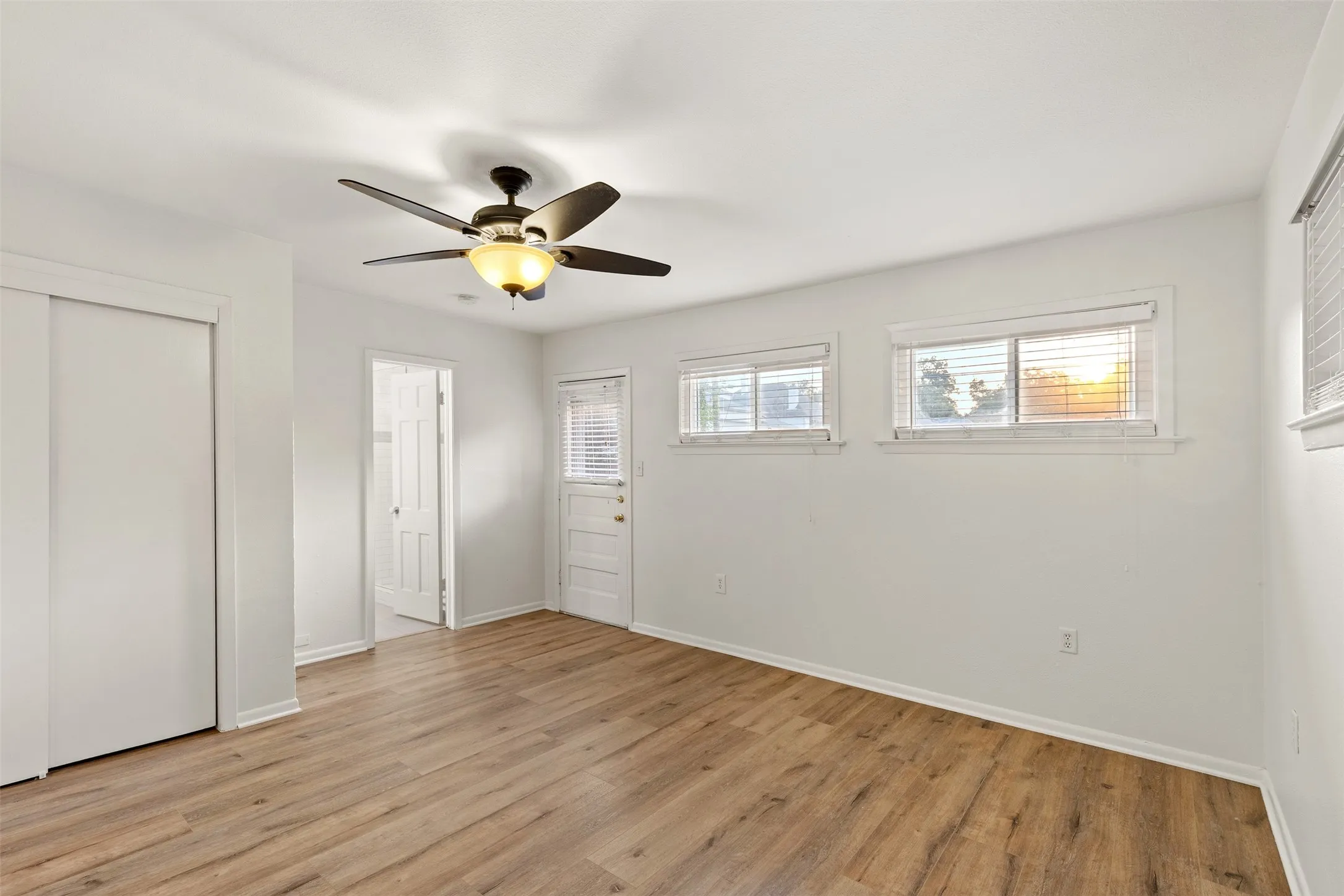 Wood-finish flooring, two windows with blinds, ceiling fan with light fixture, white walls, and a white sliding closet door