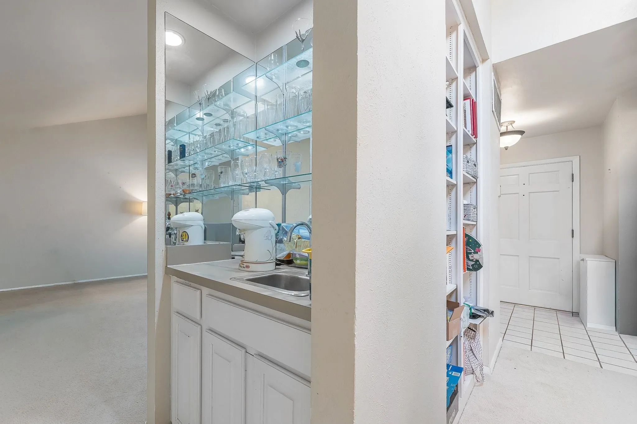 Convenient wet bar nook with mirrored backsplash, glass shelving.