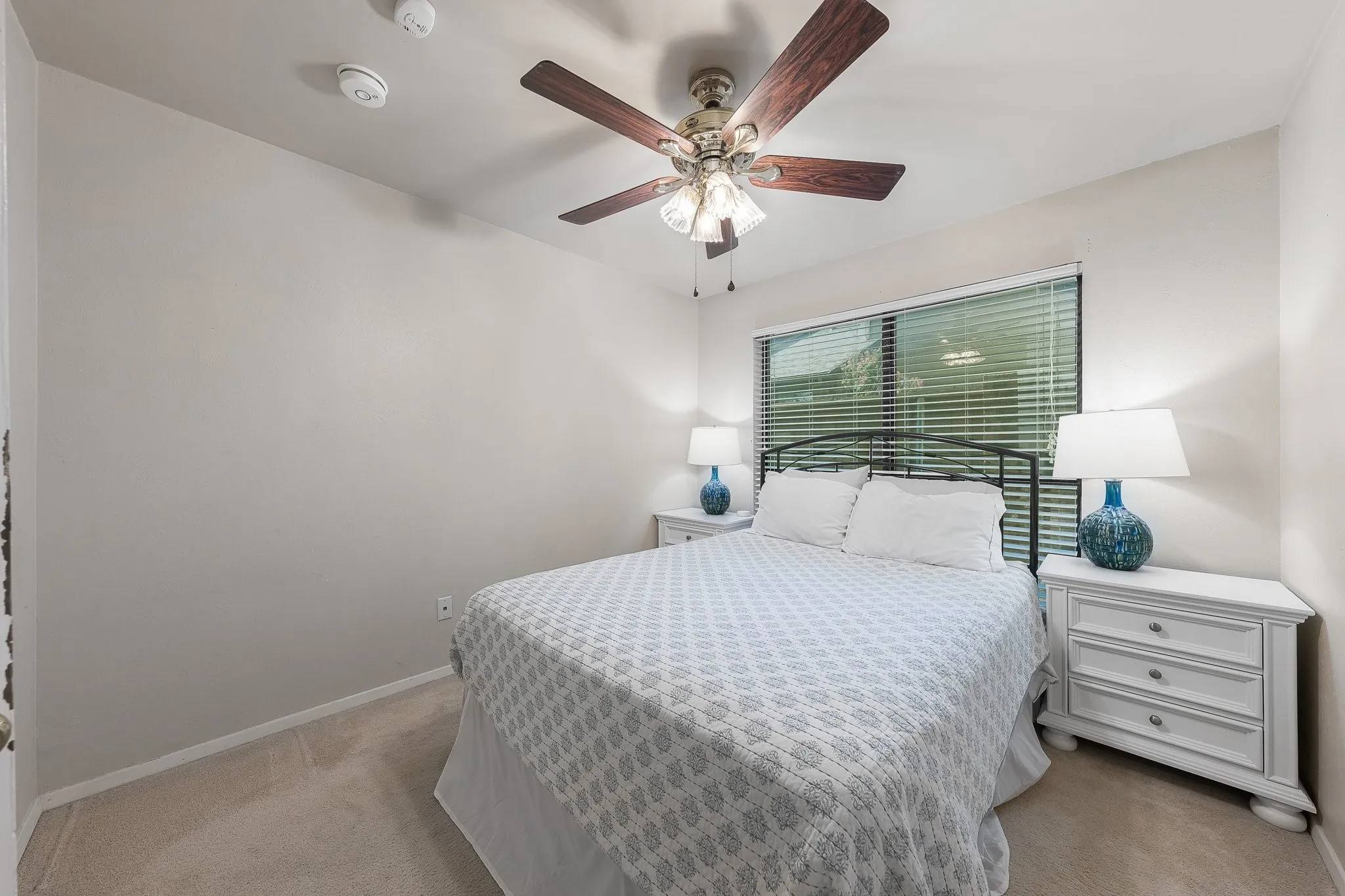 Bright guest bedroom with ceiling fan and neutral carpet.