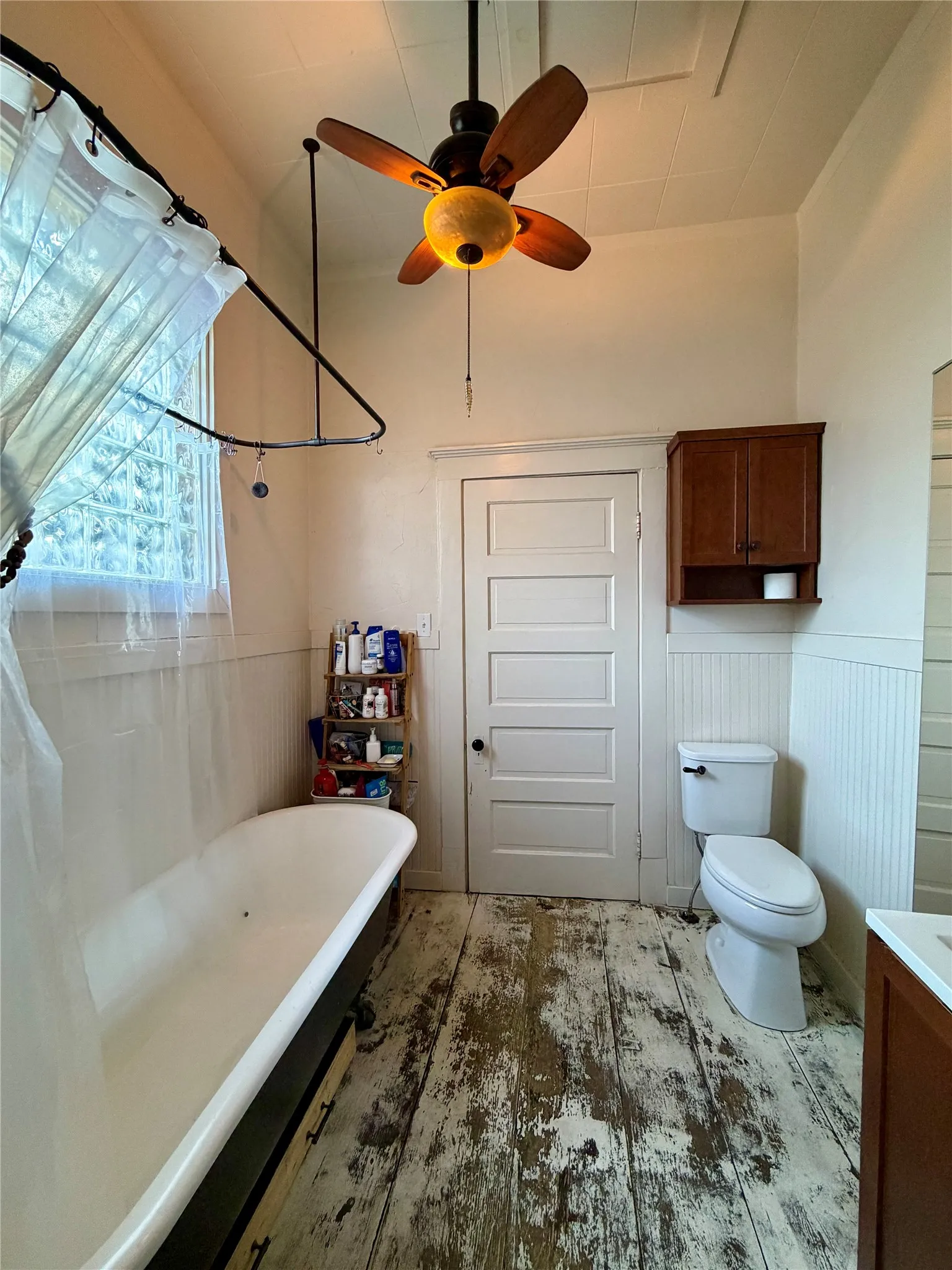 Clawfoot tub with shower curtain rod, a ceiling fan with light fixture, and distressed wood-finish flooring