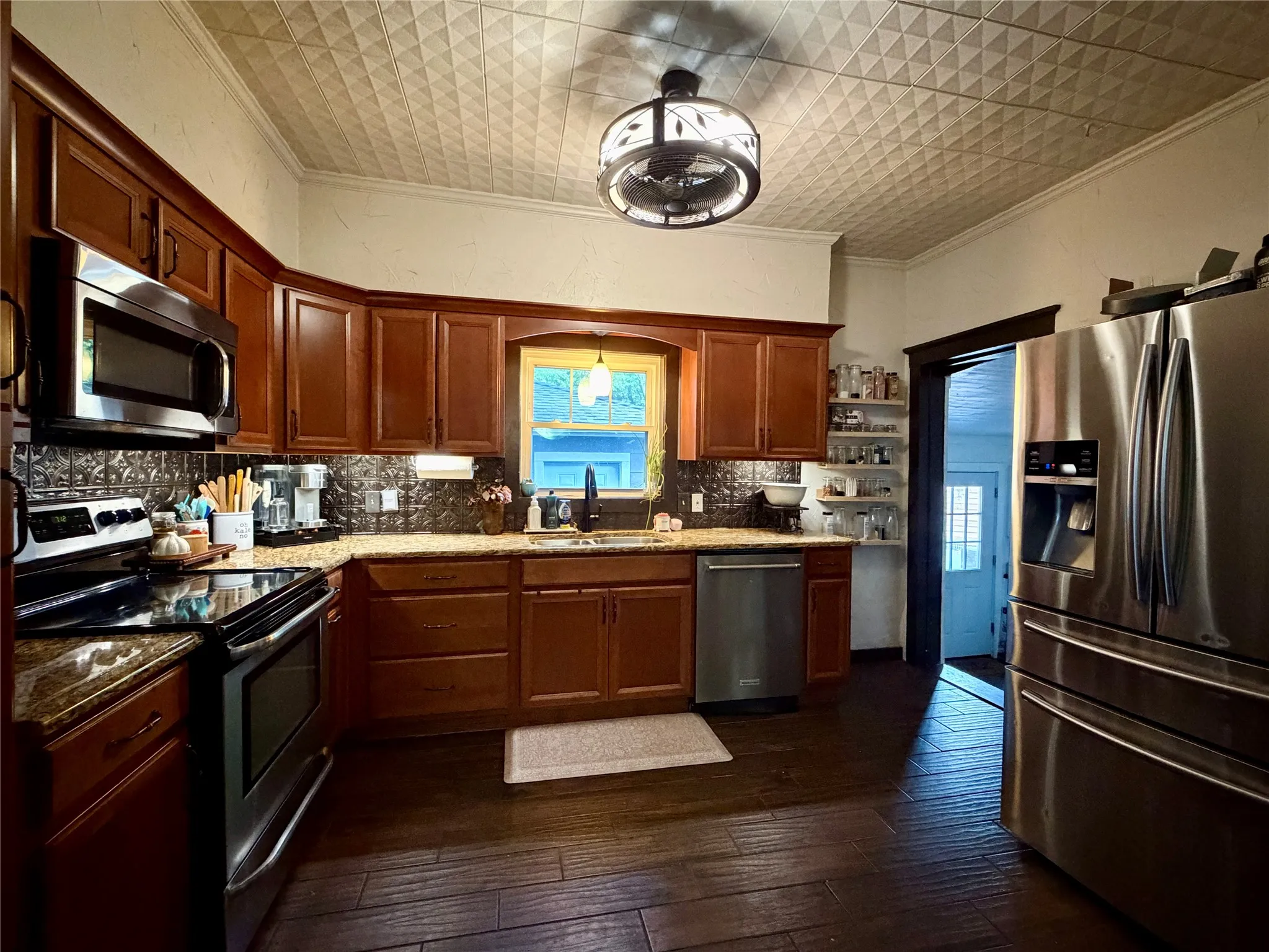 Kitchen featuring dark wood-finish flooring, L-shaped cabinetry with granite-style countertops, stainless steel appliances, a decorative ceiling with a central light fixture, and a window above the sink