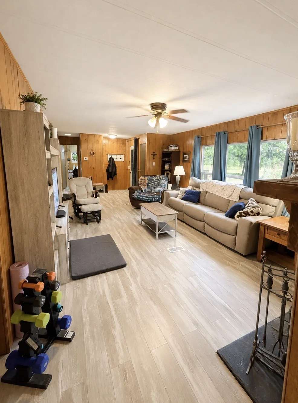 Open-concept living area with wood-finish flooring, wood paneling, and a ceiling fan