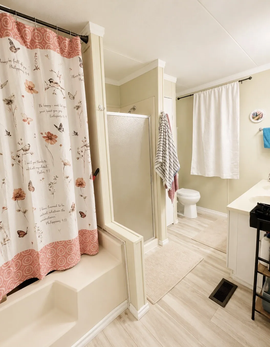 Built-in shower and tub combination, separate shower enclosure with frosted glass, wood-finish flooring, white vanity with integrated sink, and crown molding accents