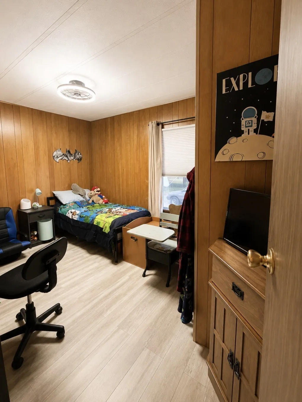 Light wood-finish flooring with wood paneling, a flush-mount ceiling light, and a window with blinds