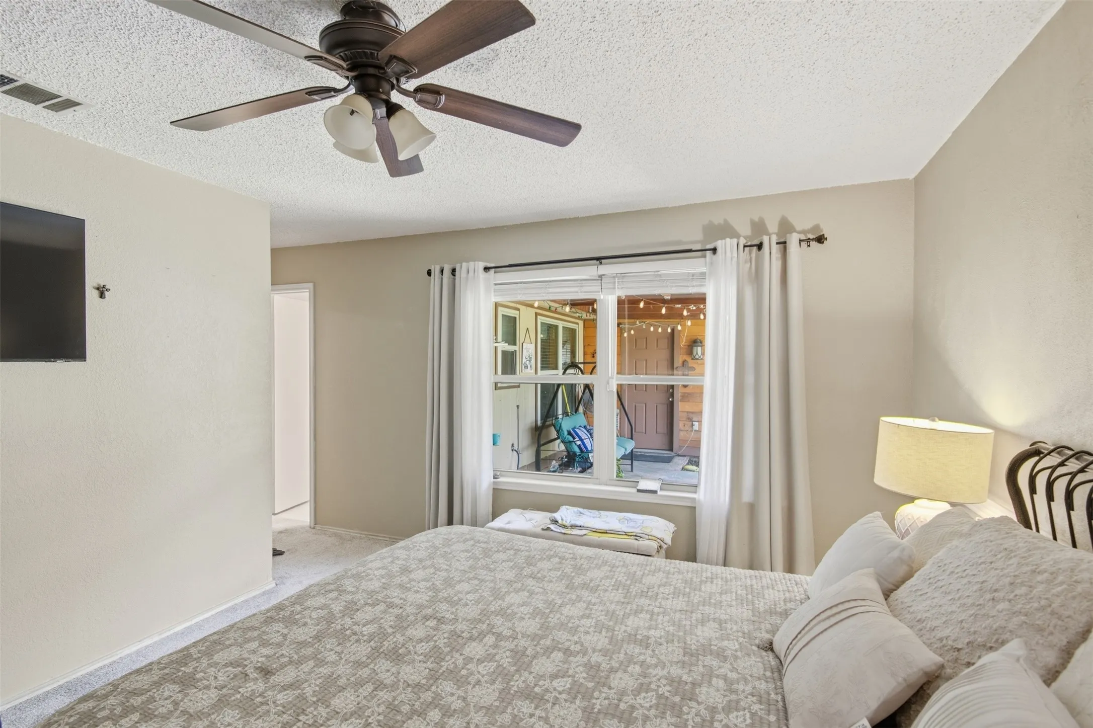 Bedroom featuring a ceiling fan with integrated lighting, textured ceilings, a window with curtains, and neutral-toned wall paint