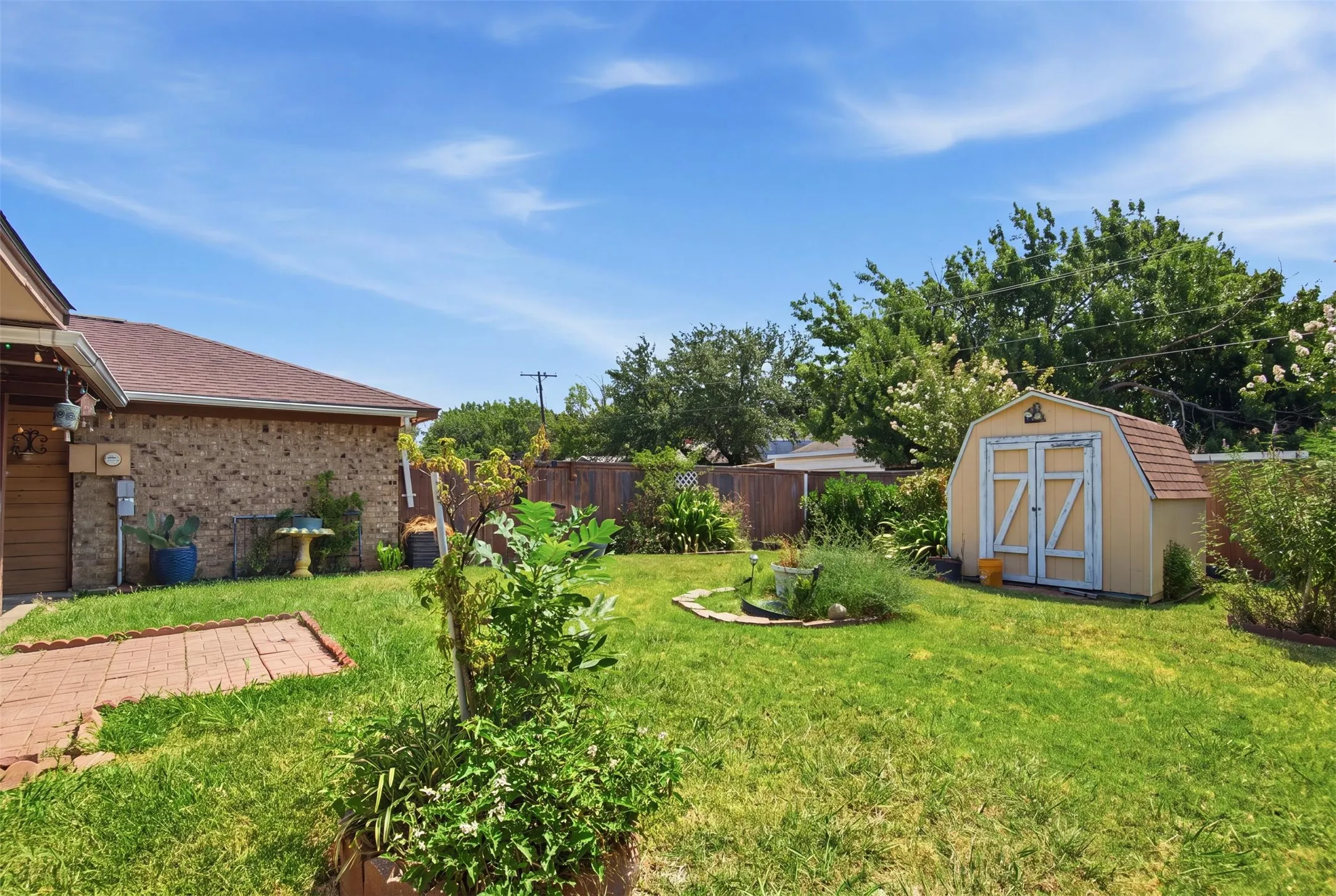 Expansive backyard featuring a manicured lawn, a detached storage shed, perimeter fencing, and mature trees