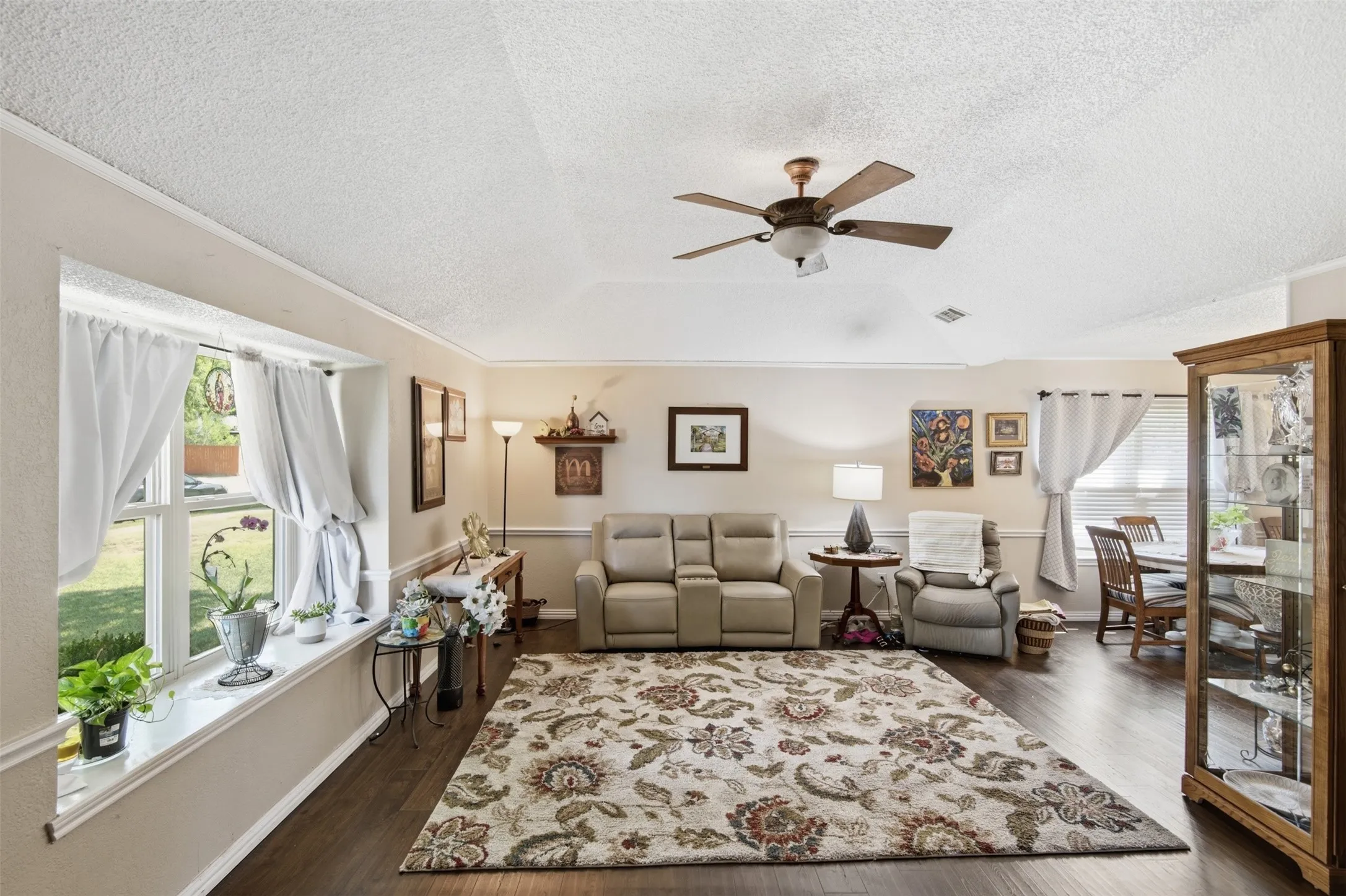 Spacious living area featuring wood-finish flooring, a ceiling fan, and decorative crown molding
