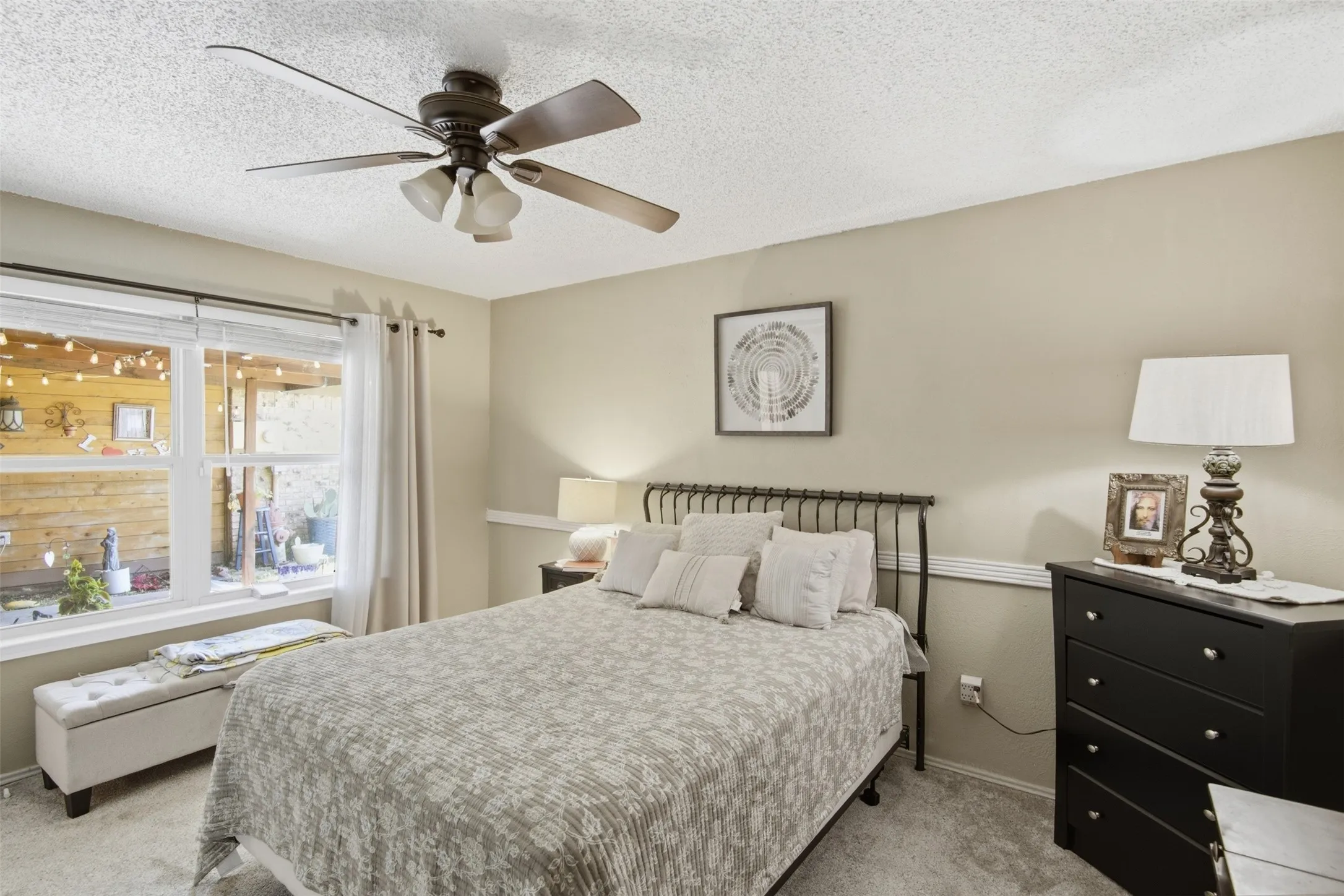 Carpeted room featuring a ceiling fan with integrated lighting, neutral wall paint, and a large window overlooking a wooden fence