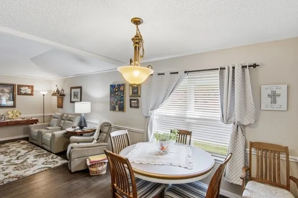 Open-concept living and dining area featuring wood-finish flooring, a pendant light fixture, and an oval dining table with wood chairs