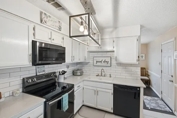 Kitchen featuring white cabinetry, subway tile backsplash, light-toned countertops, a black electric range, and a coordinating over-the-range microwave